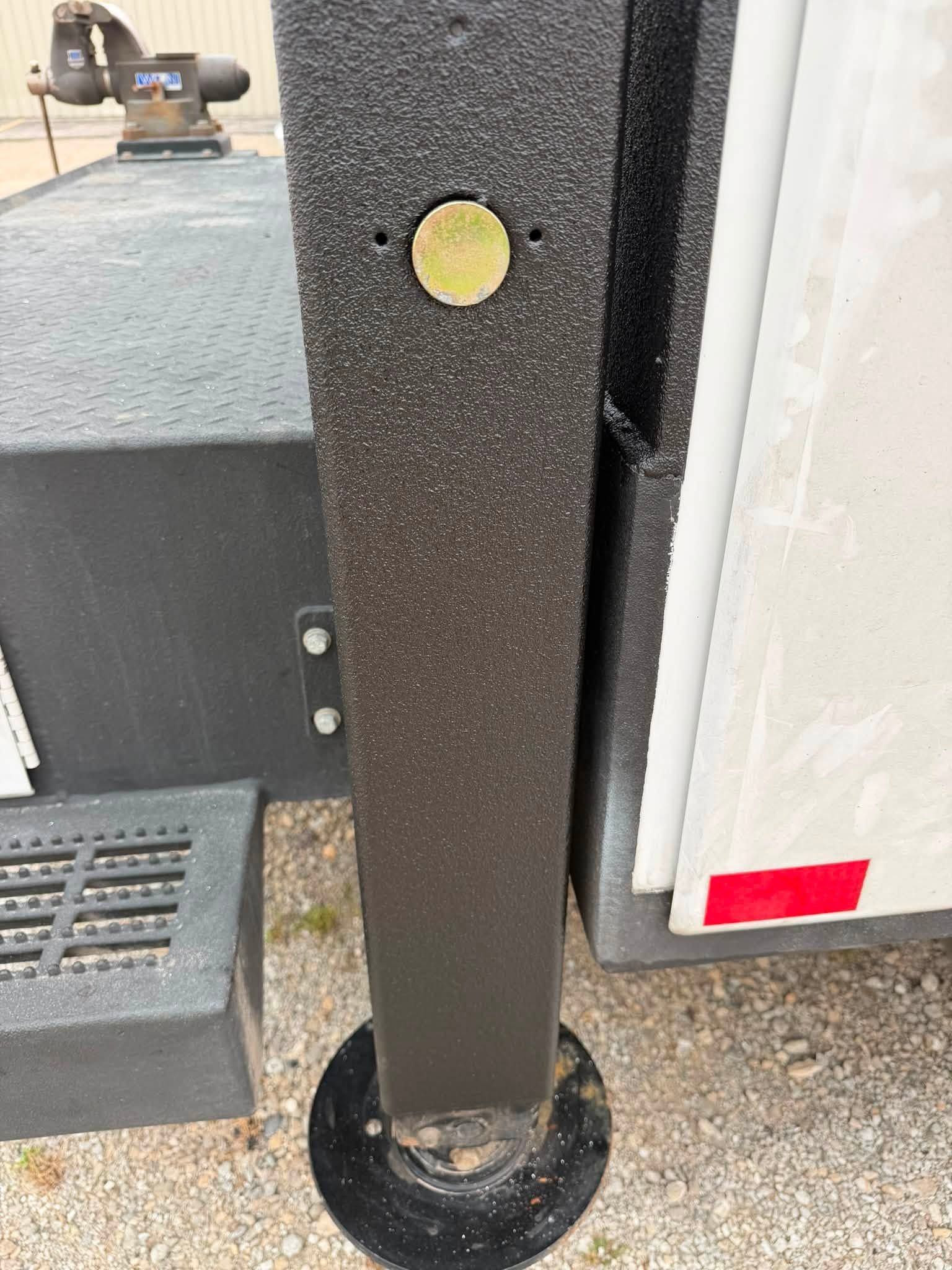 Black textured post with a yellow reflective dot beside a white trailer, on gravel.