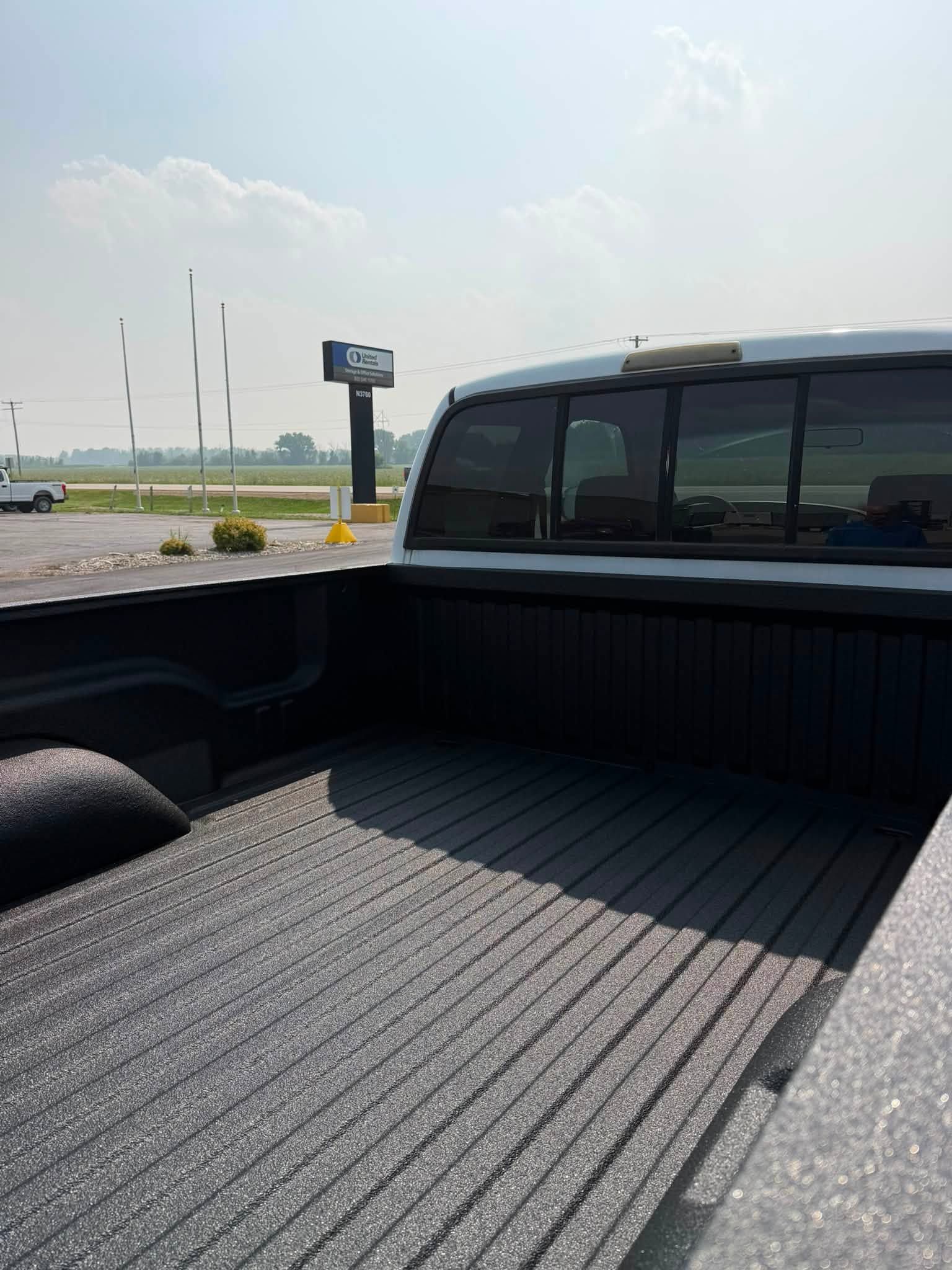 Open pickup truck bed with black bed liner parked near a roadway under a clear sky