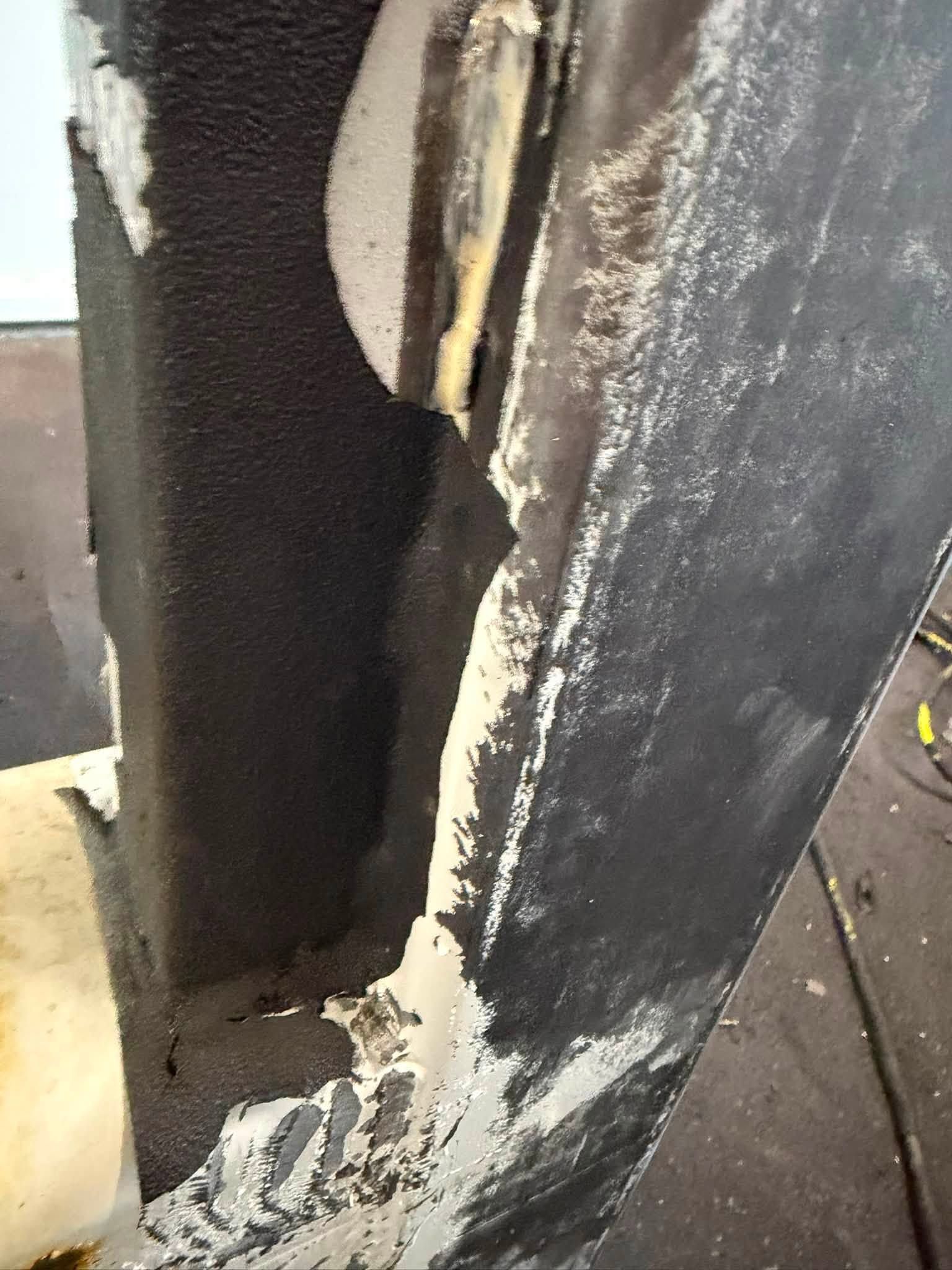 Close-up of a damaged black painted surface with a large vertical crack and chipped white edges.