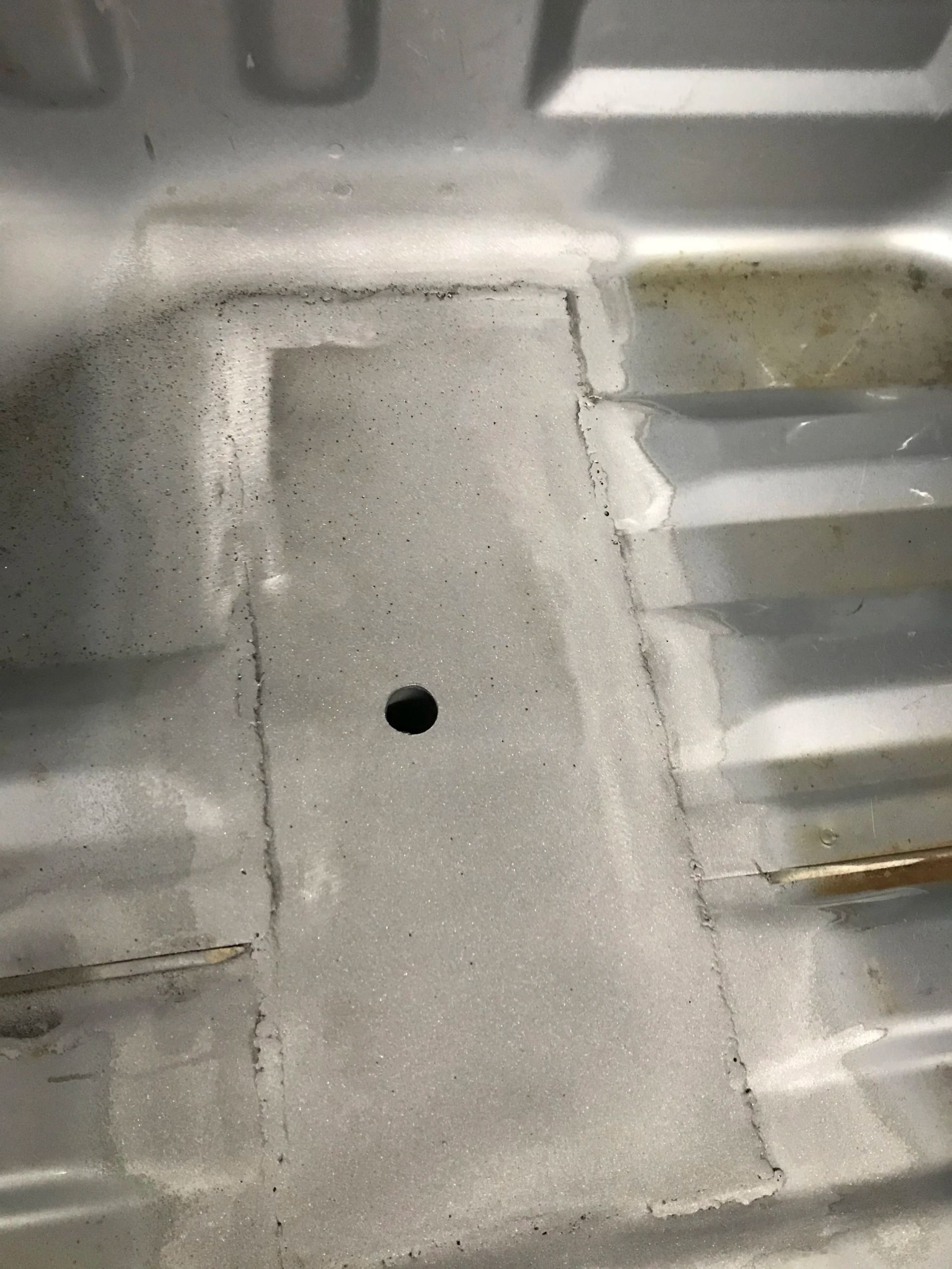 Close-up of a gray metal surface with a small round hole in the center and visible seams.