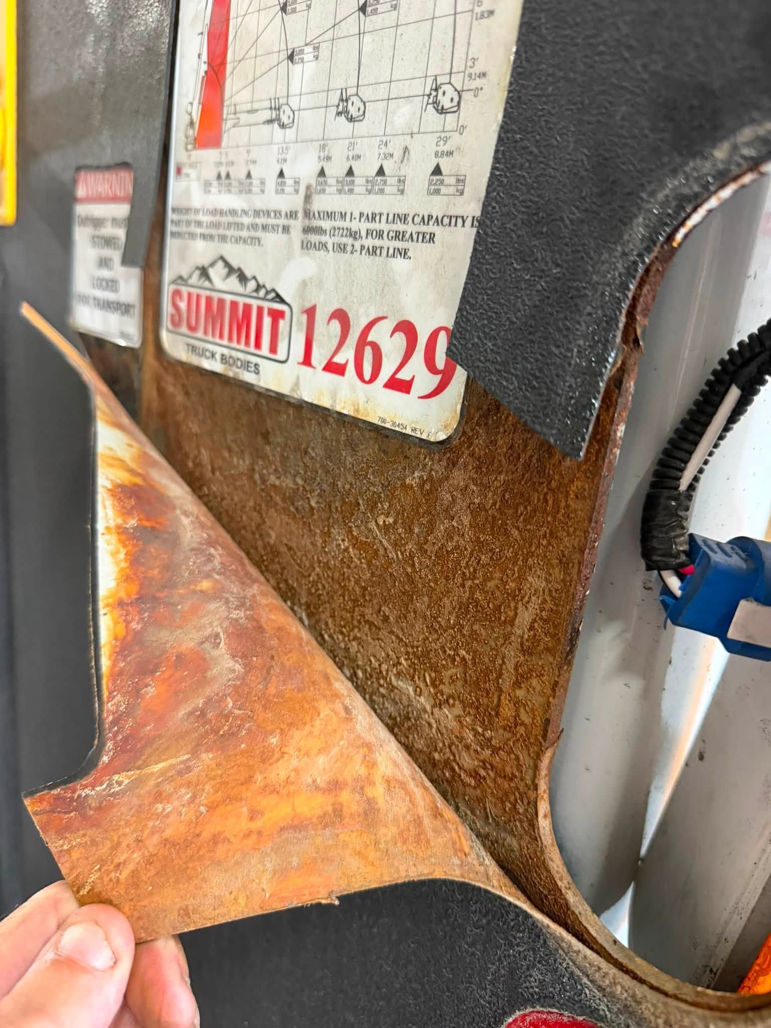 A hand peeling back rusty orange insulation from a metal appliance label reading “SUMMIT 12629.”
