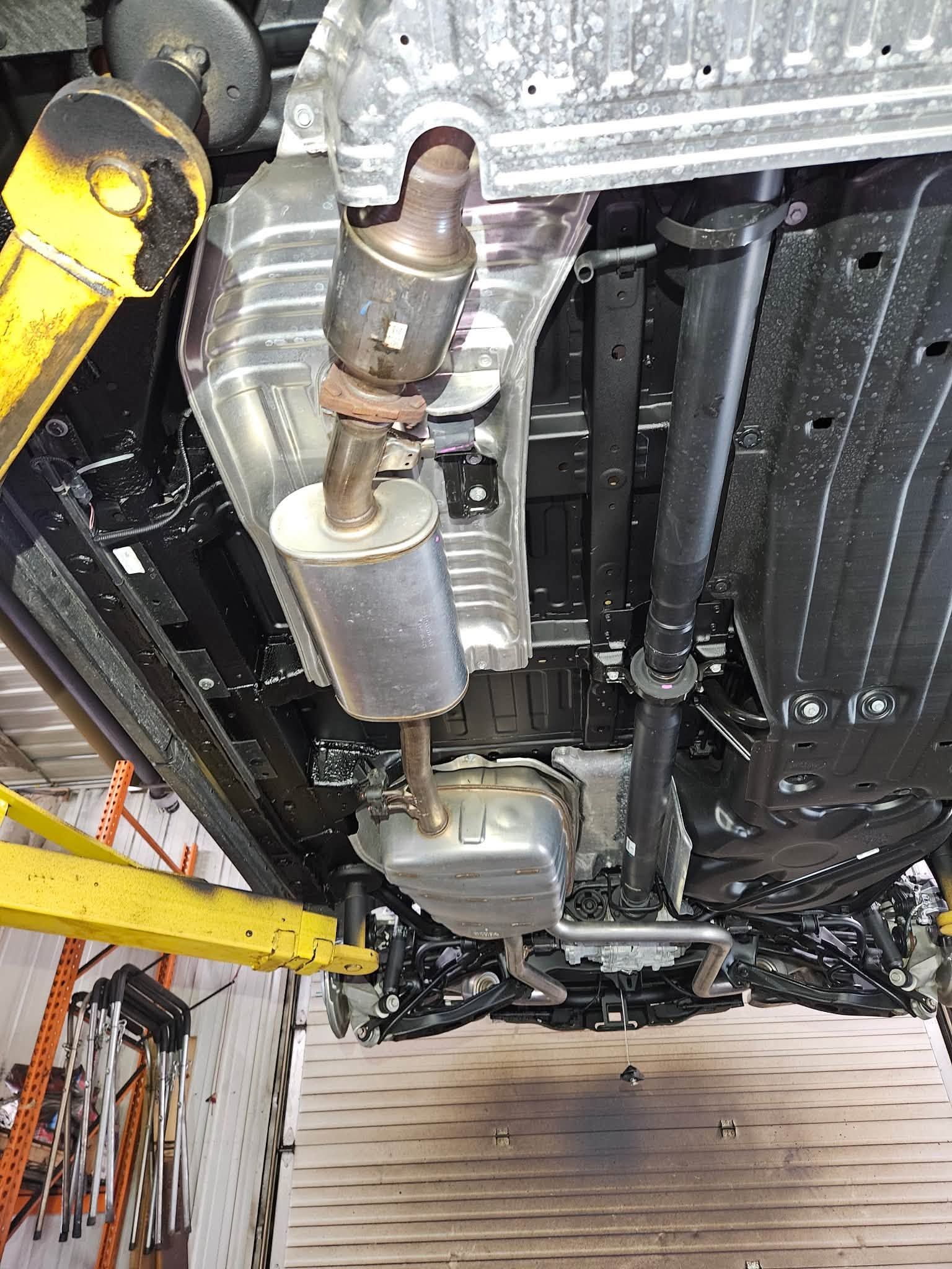 Undercarriage of a car on a lift, showing exhaust and suspension components in a garage.