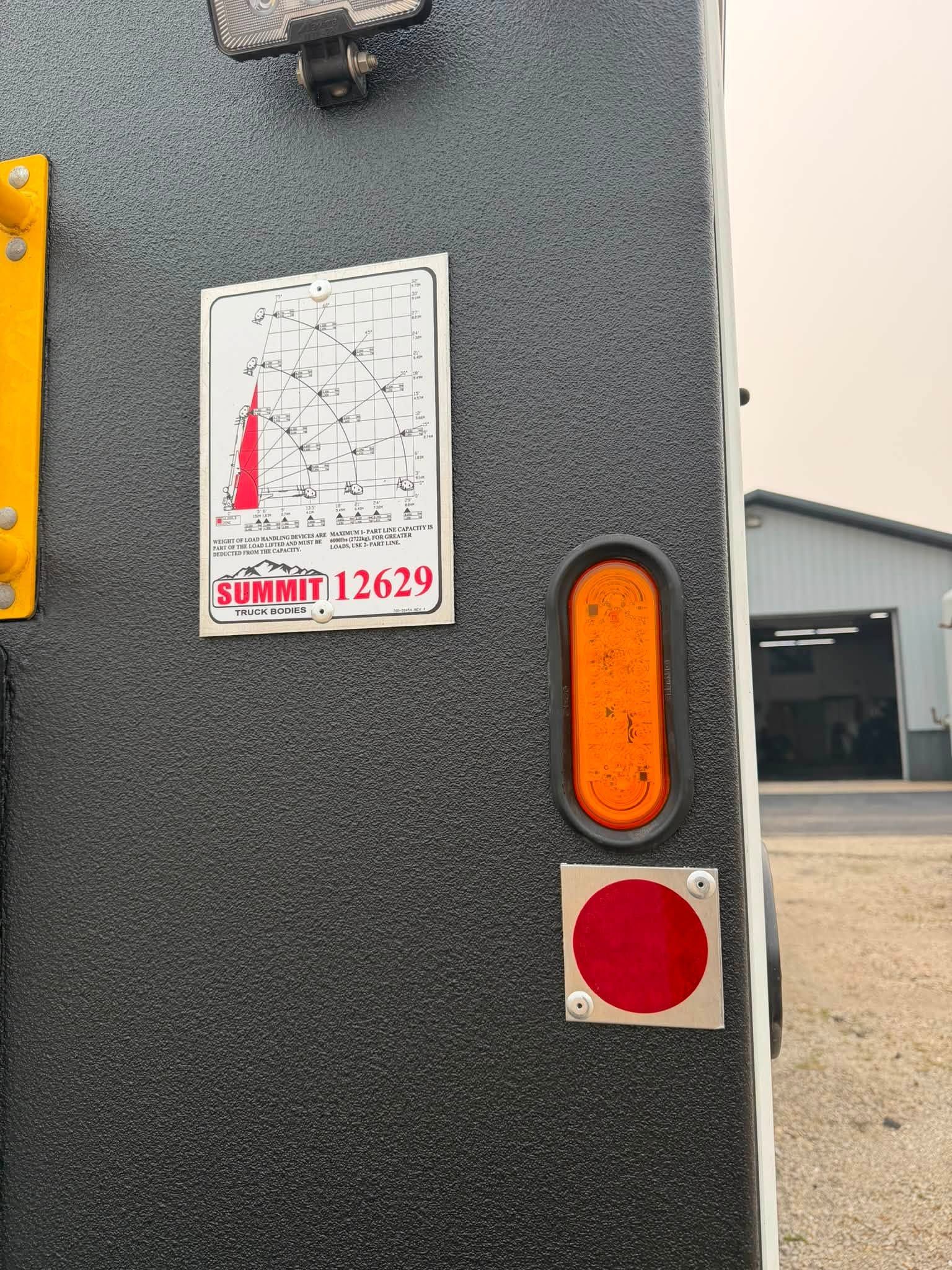 Close-up of a gray trailer door with an orange reflector, red stop circle, and warning sticker.