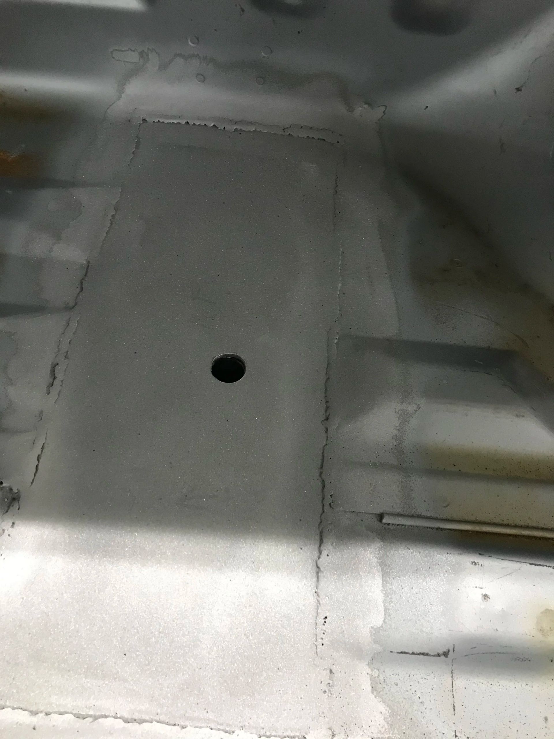 Gray metal surface with a small round hole in the center and shallow ridges on the sides