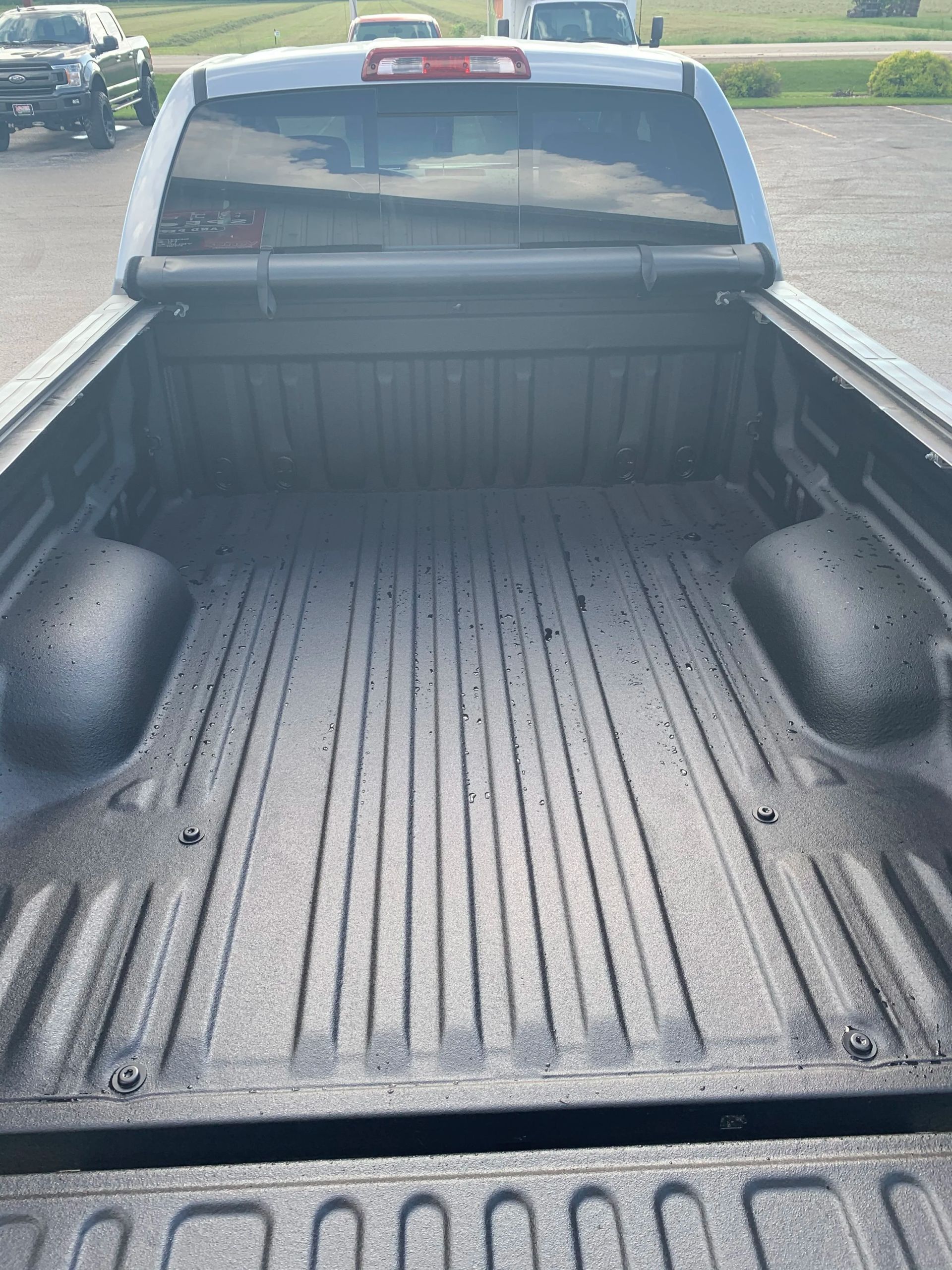 Empty pickup truck bed with black liner, viewed from the tailgate in a parking lot.