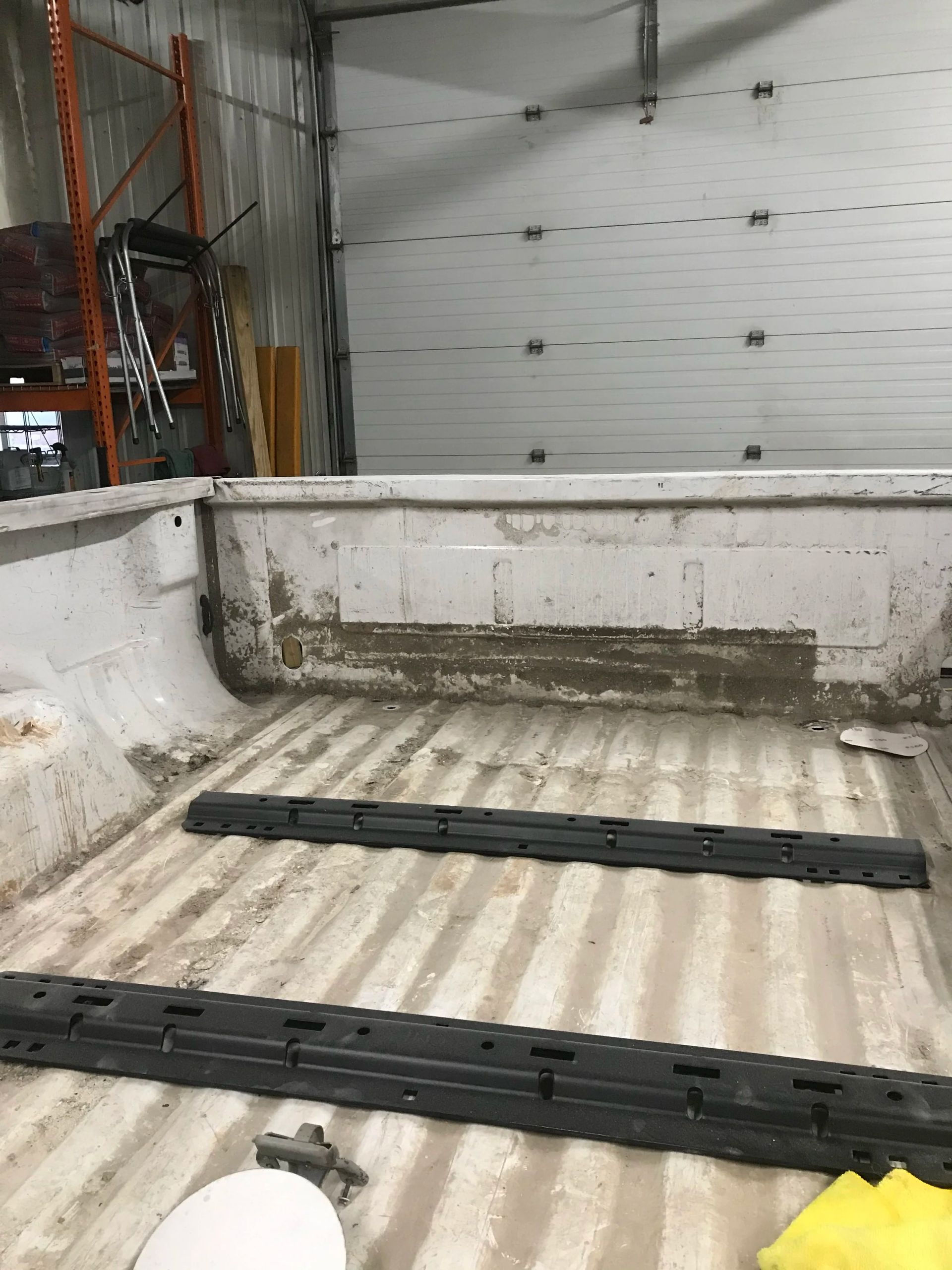 Empty white pickup truck bed inside a garage, with black bed liner strips and closed garage door in back
