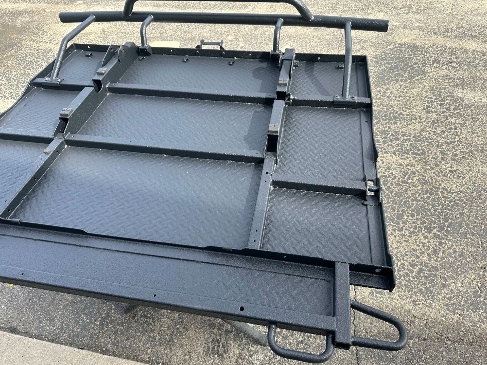 Black metal cargo rack or roof platform with straps, lying on pavement outdoors