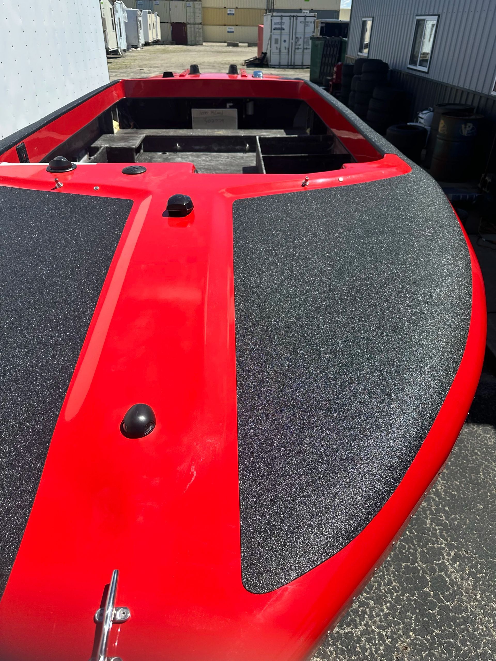 Red boat deck with black textured panels, viewed from above in a marina.