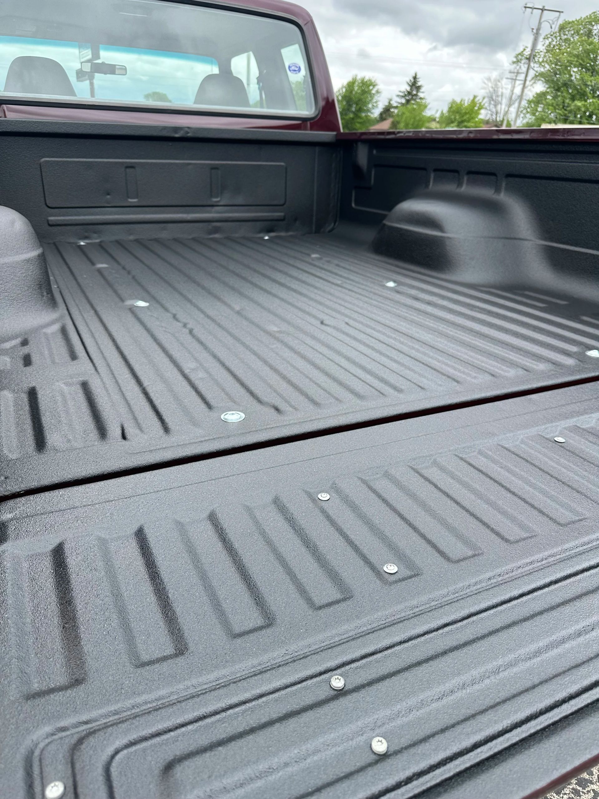 Empty black pickup truck bed with ribbed liner and red cab, viewed from the tailgate.