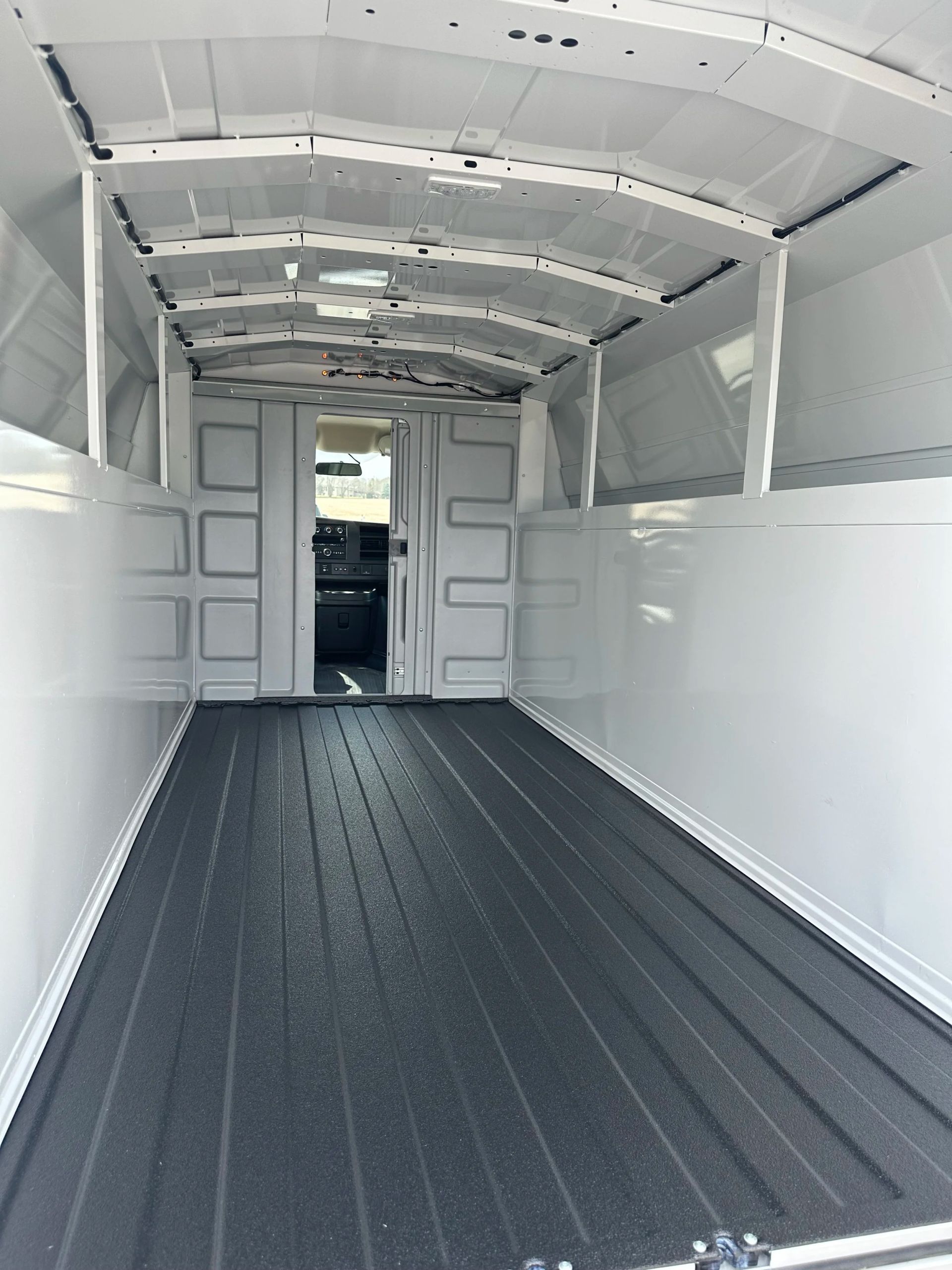 Empty white cargo van interior with black ribbed floor and open rear doors