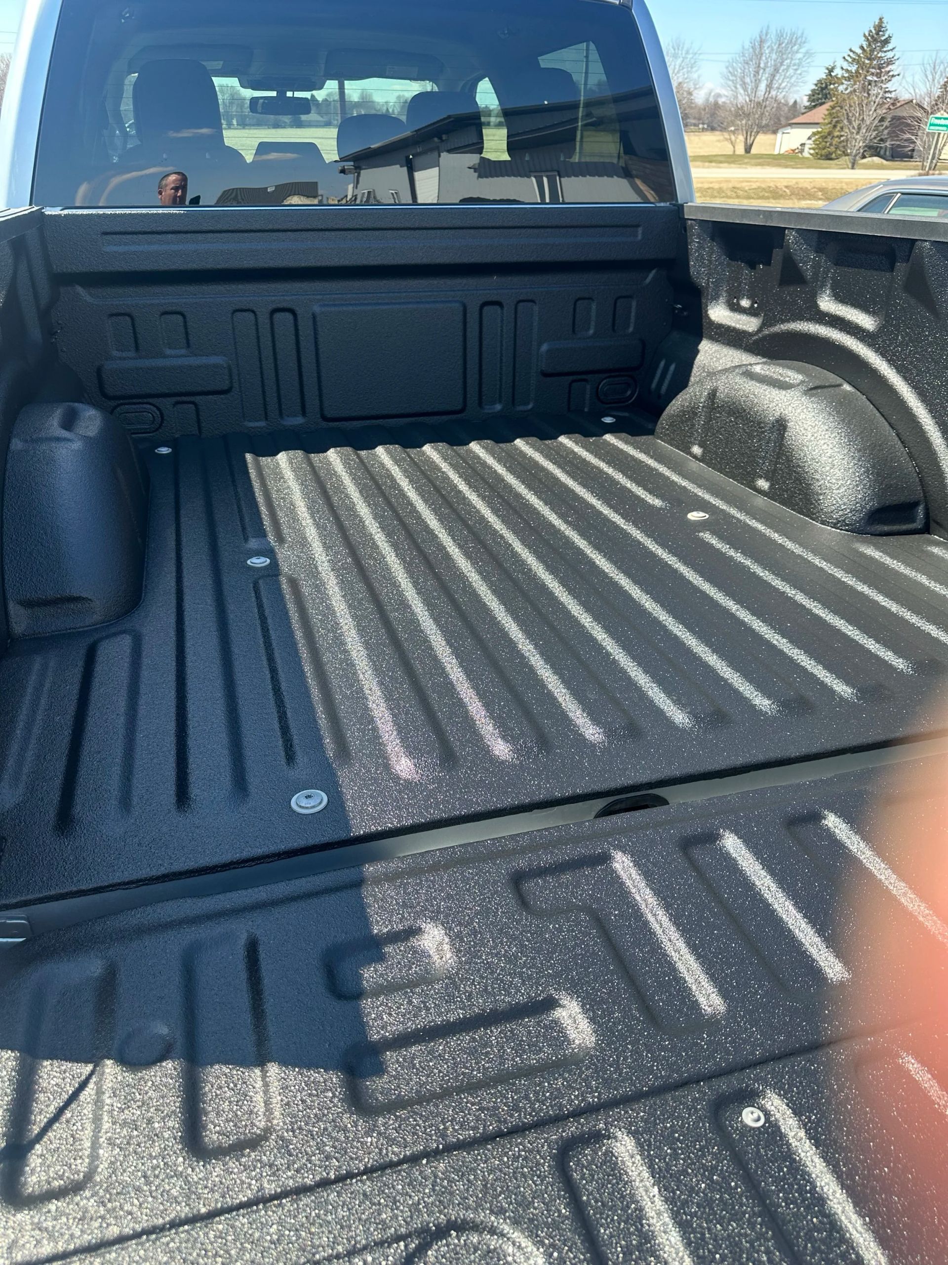 Pickup truck bed lined with black textured spray-in liner, viewed from the tailgate.