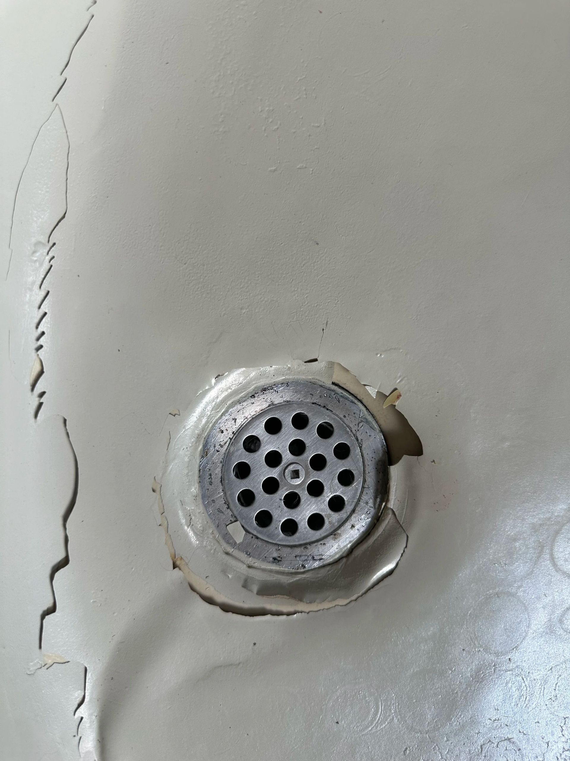 Close-up of a silver drain with holes on a light gray metal surface, beside a crack on the left