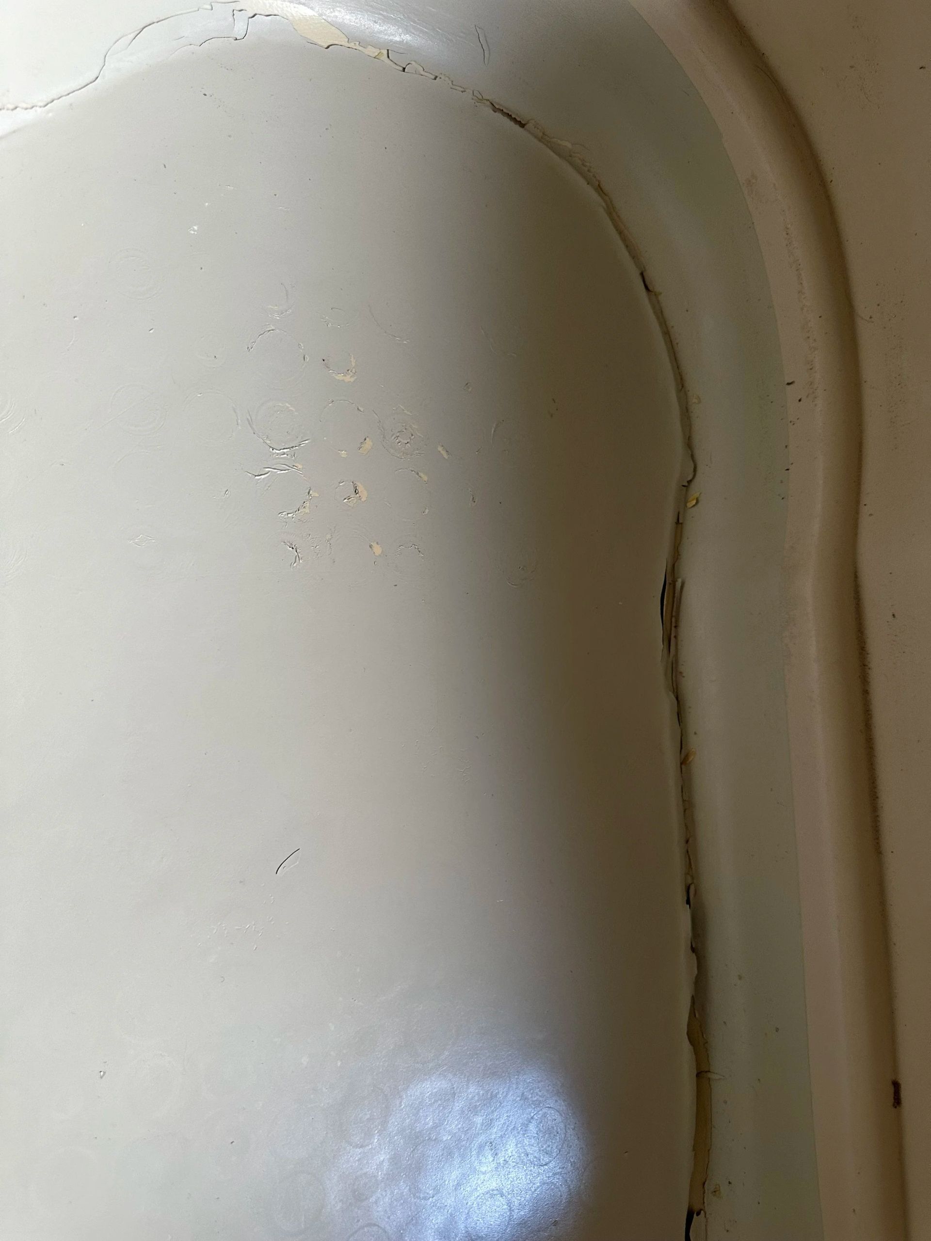 Close-up of a white curved surface with a dark seam and small specks of grime
