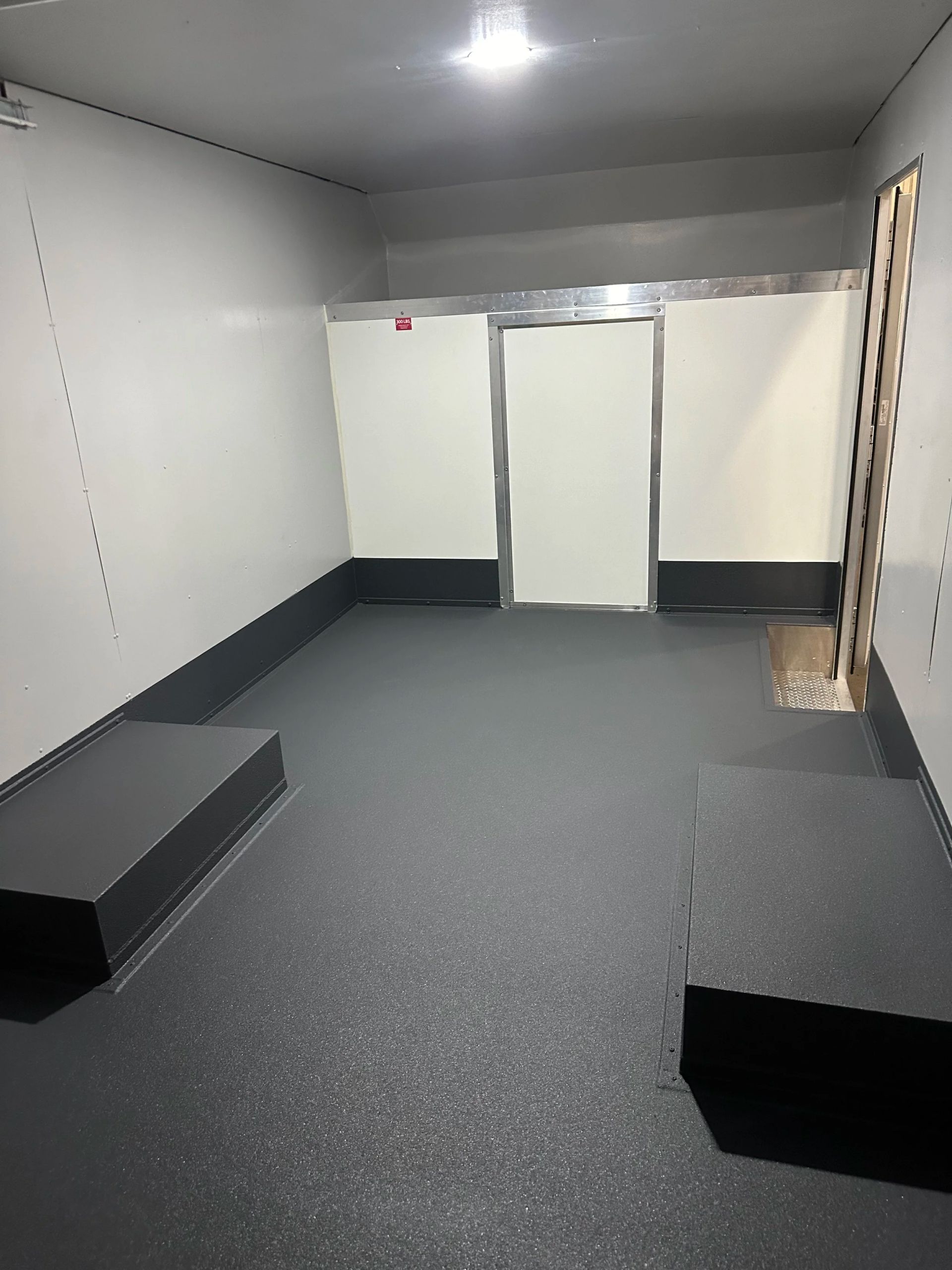 Empty gray room with white walls, dark floor, and two black benches near the corners