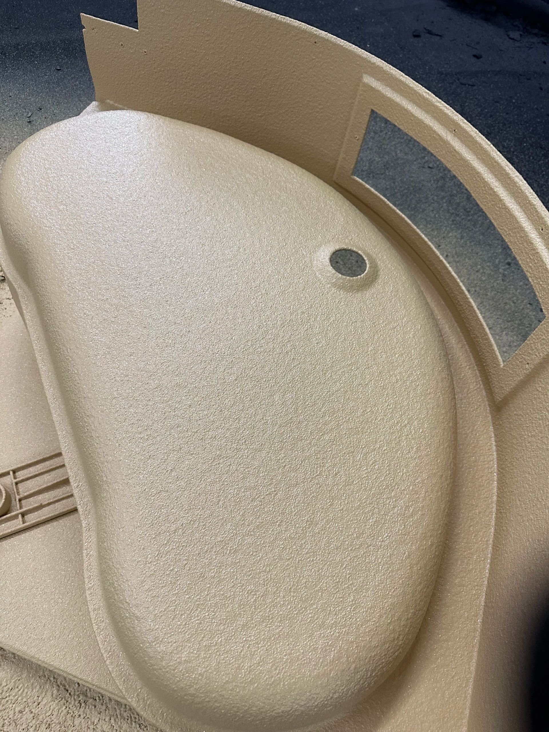 Beige textured sink with a round drain and a curved cardboard or plastic divider beside it