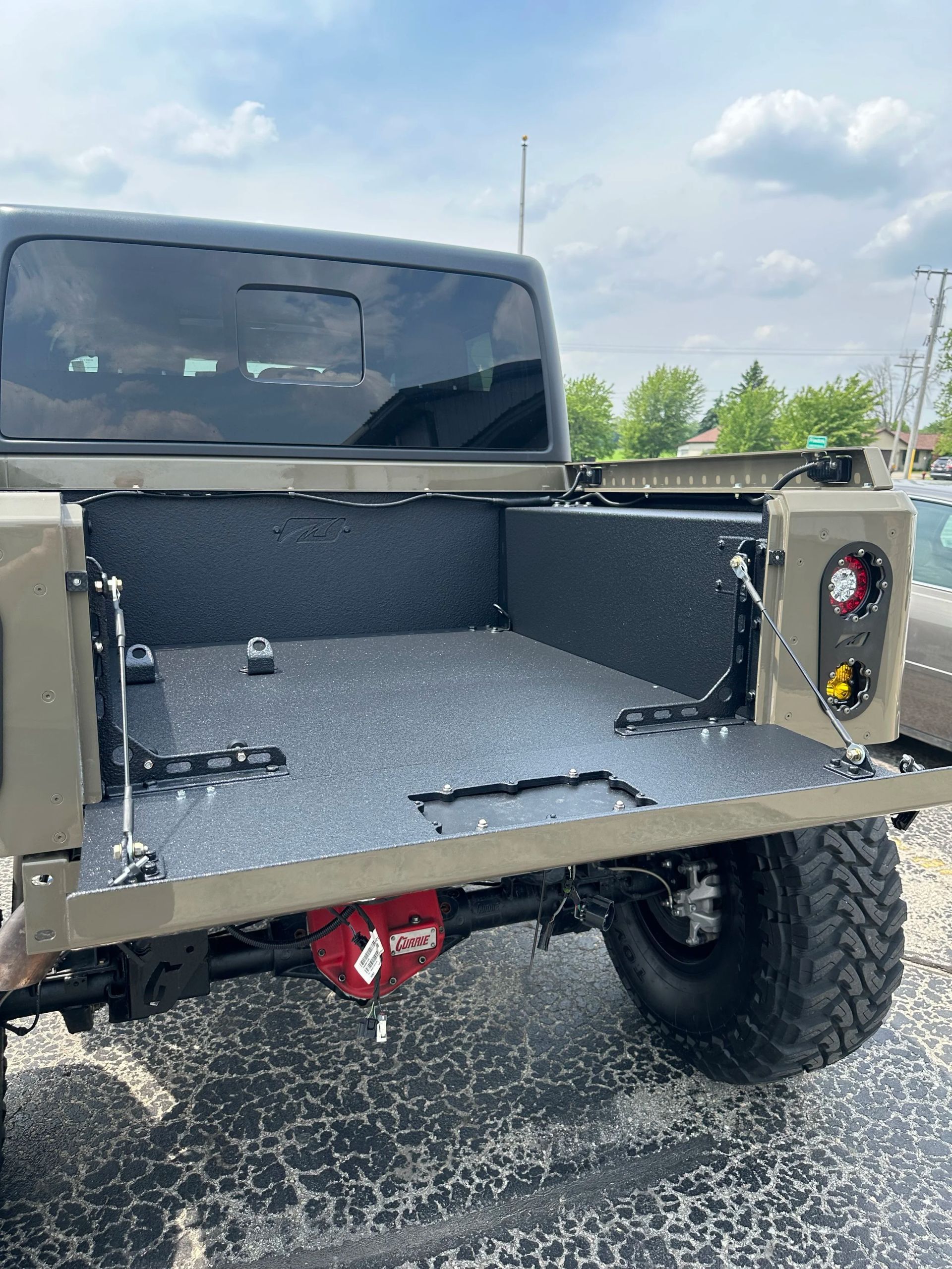 Open pickup truck bed with gray carpet liner and tailgate down, parked on a paved lot under a cloudy sky