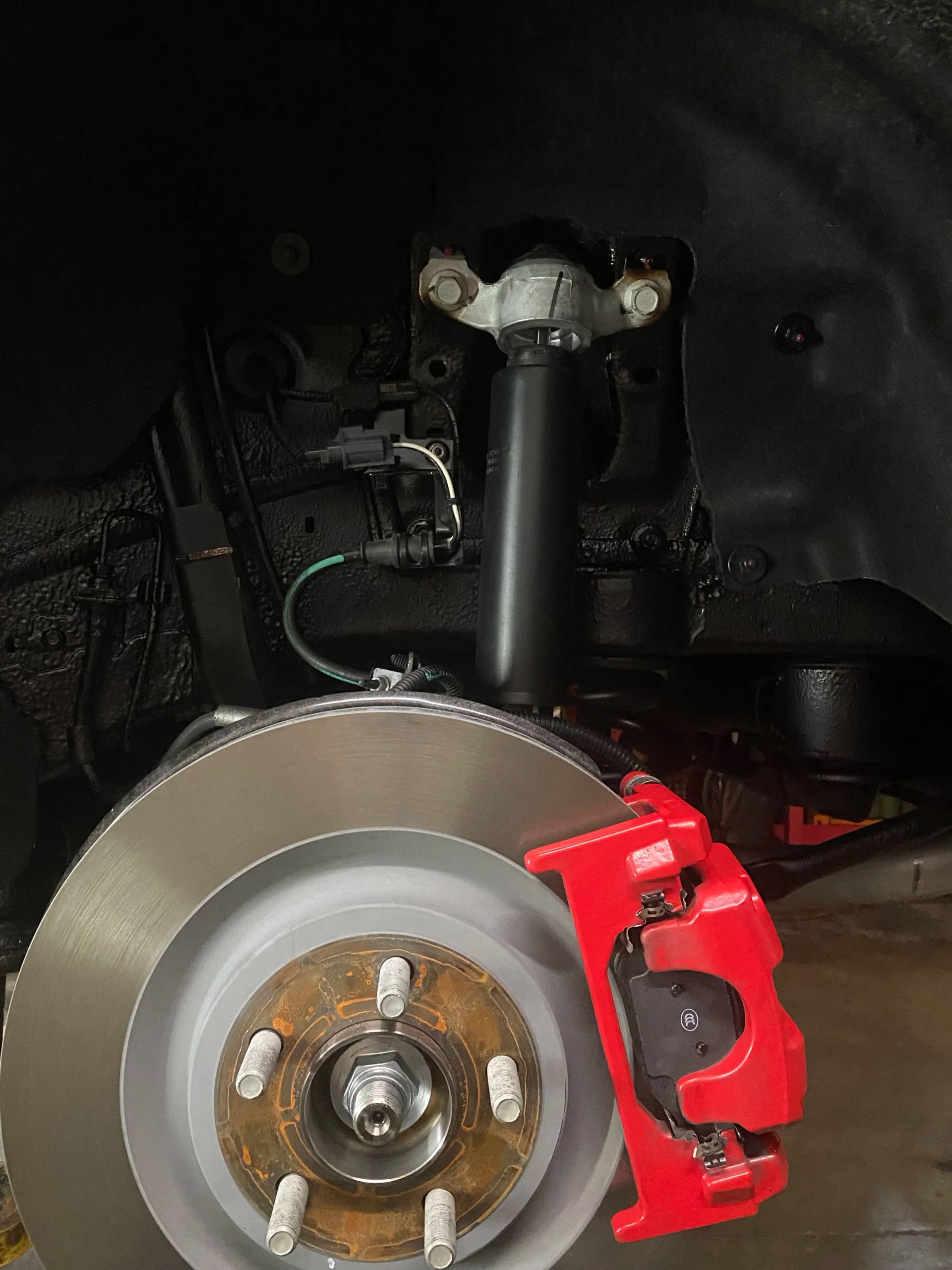 Close-up of a car brake rotor and red caliper inside the wheel well.