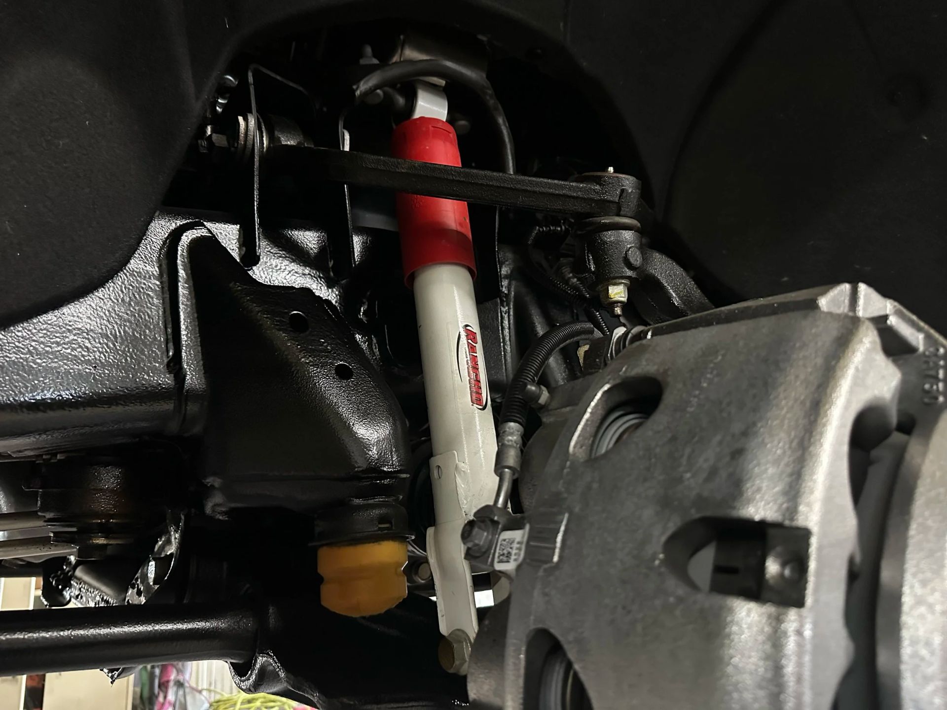 Close-up of a car suspension with a white and red shock absorber and silver brake caliper.