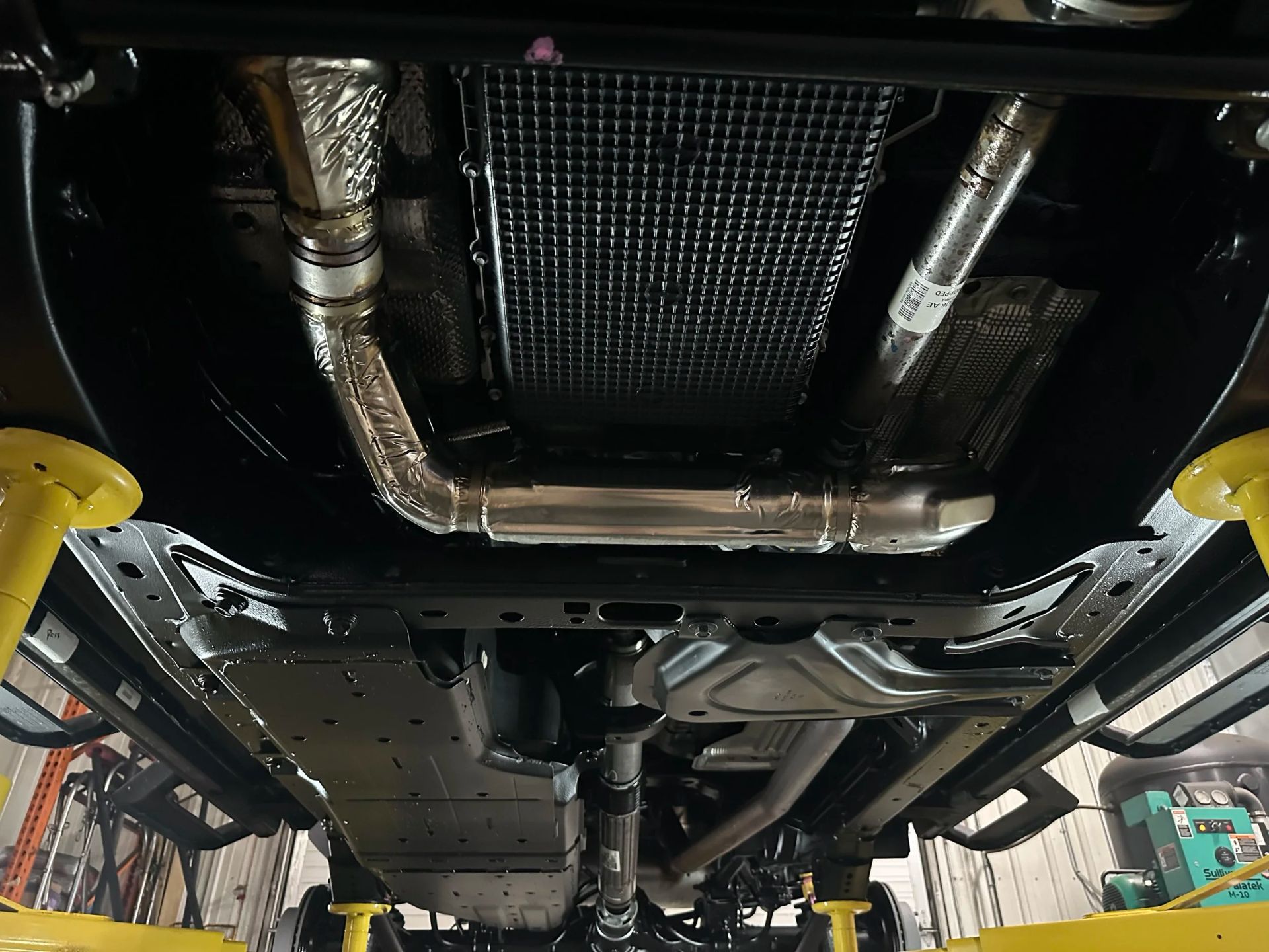 Undercarriage of a car on a lift, showing the exhaust system and metal underbody panels
