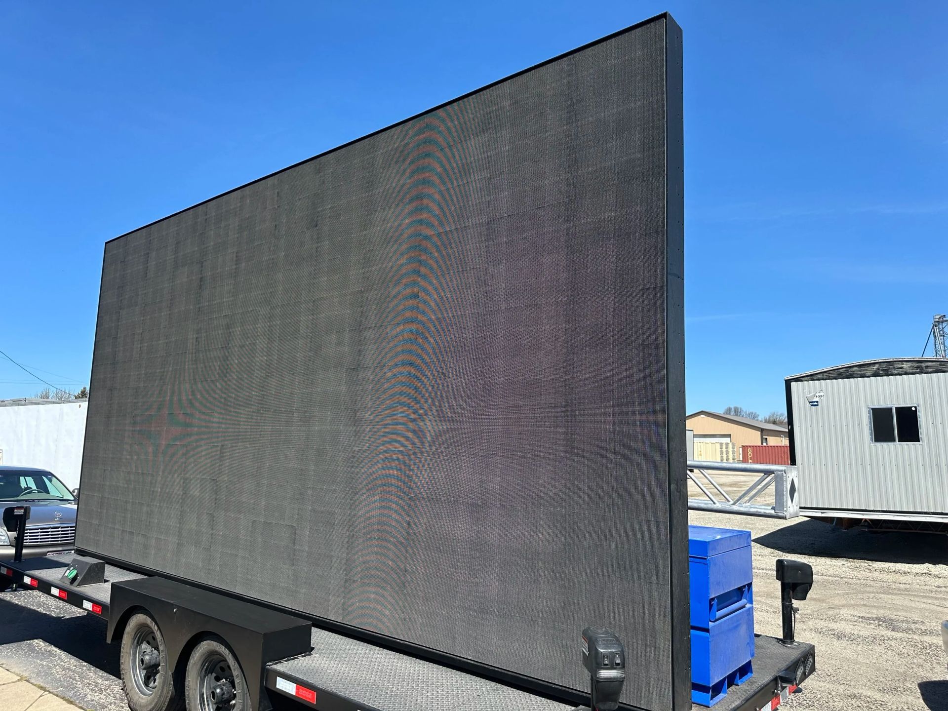 Large black LED display panel on a trailer in a parking lot under a blue sky