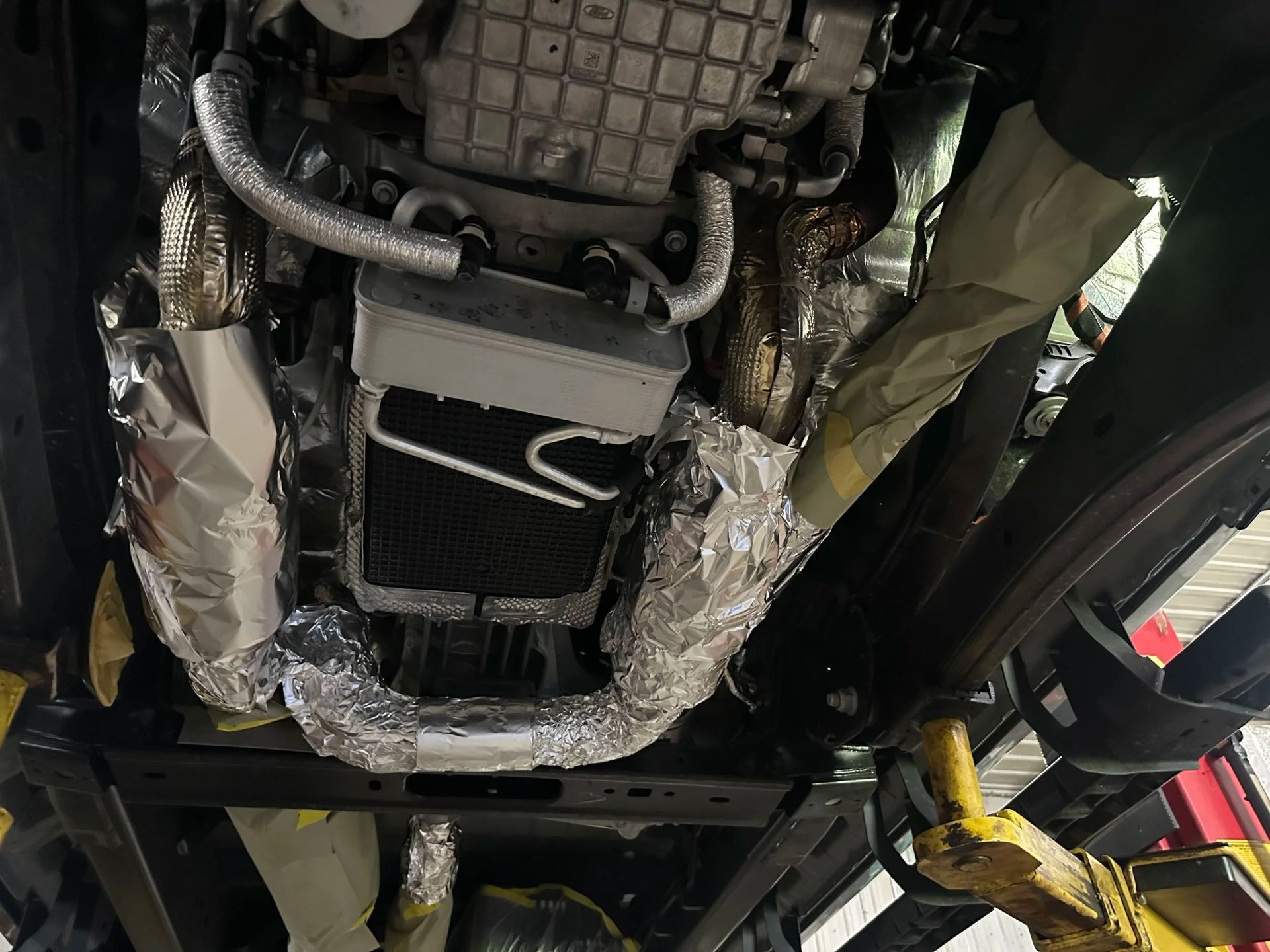 Undercarriage of a vehicle on a lift, with exposed metal parts and wrapped exhaust components.