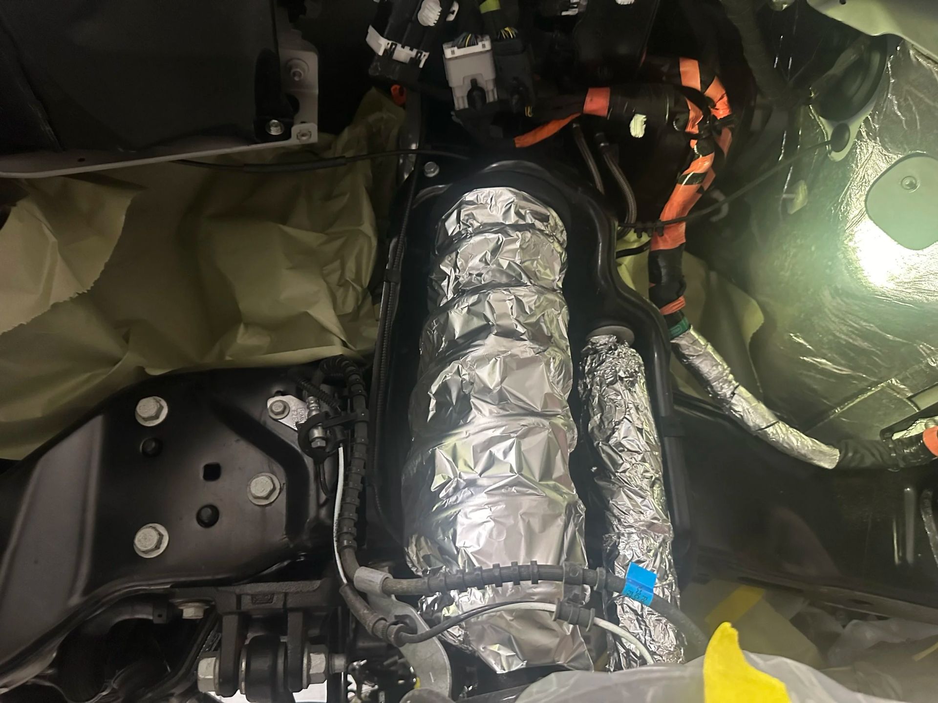 Wrapped metallic tube inside a cramped, dimly lit equipment compartment with black bags and wires