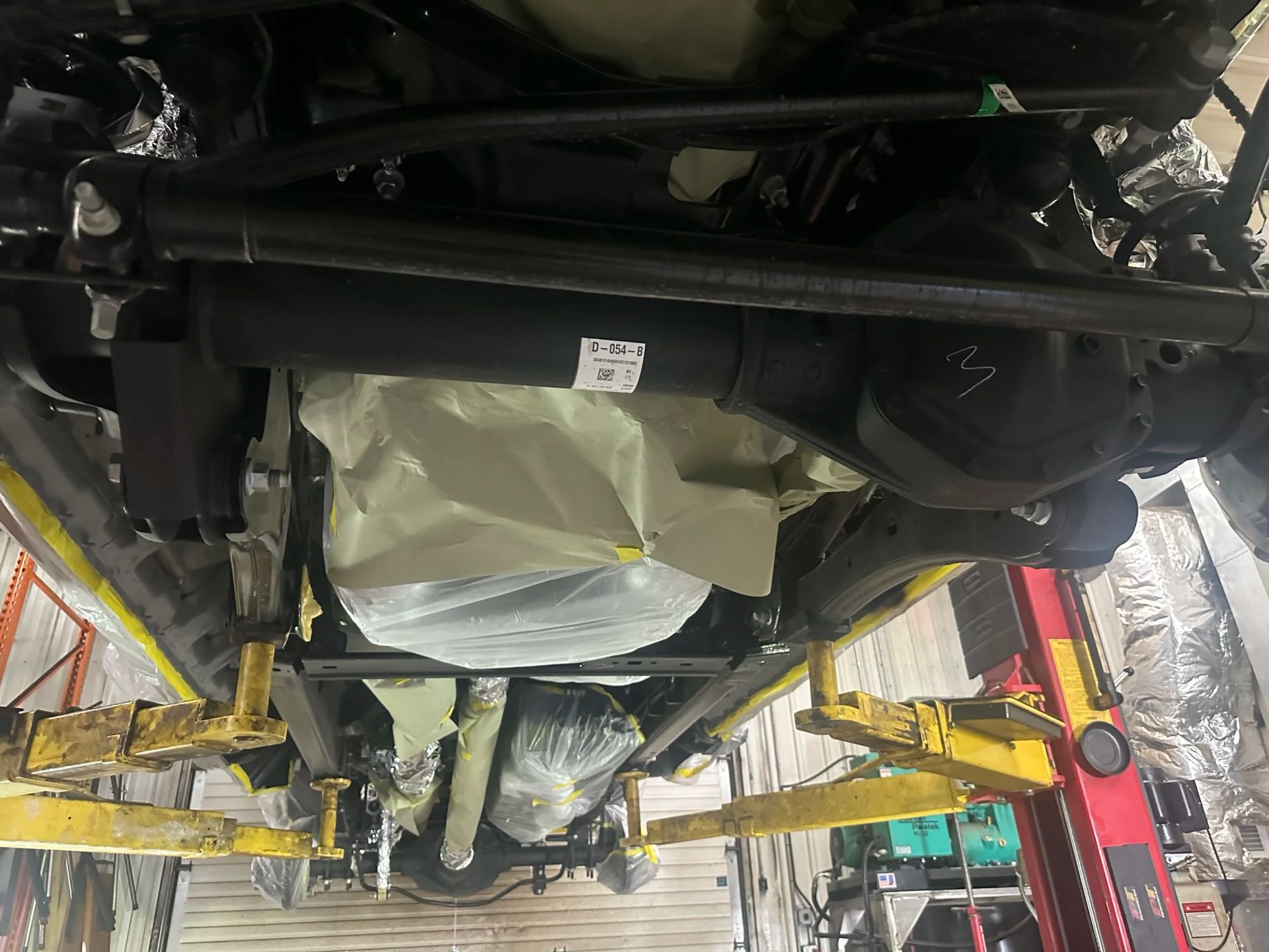 Undercarriage of a car on a lift, showing the exhaust and protective covering underneath.