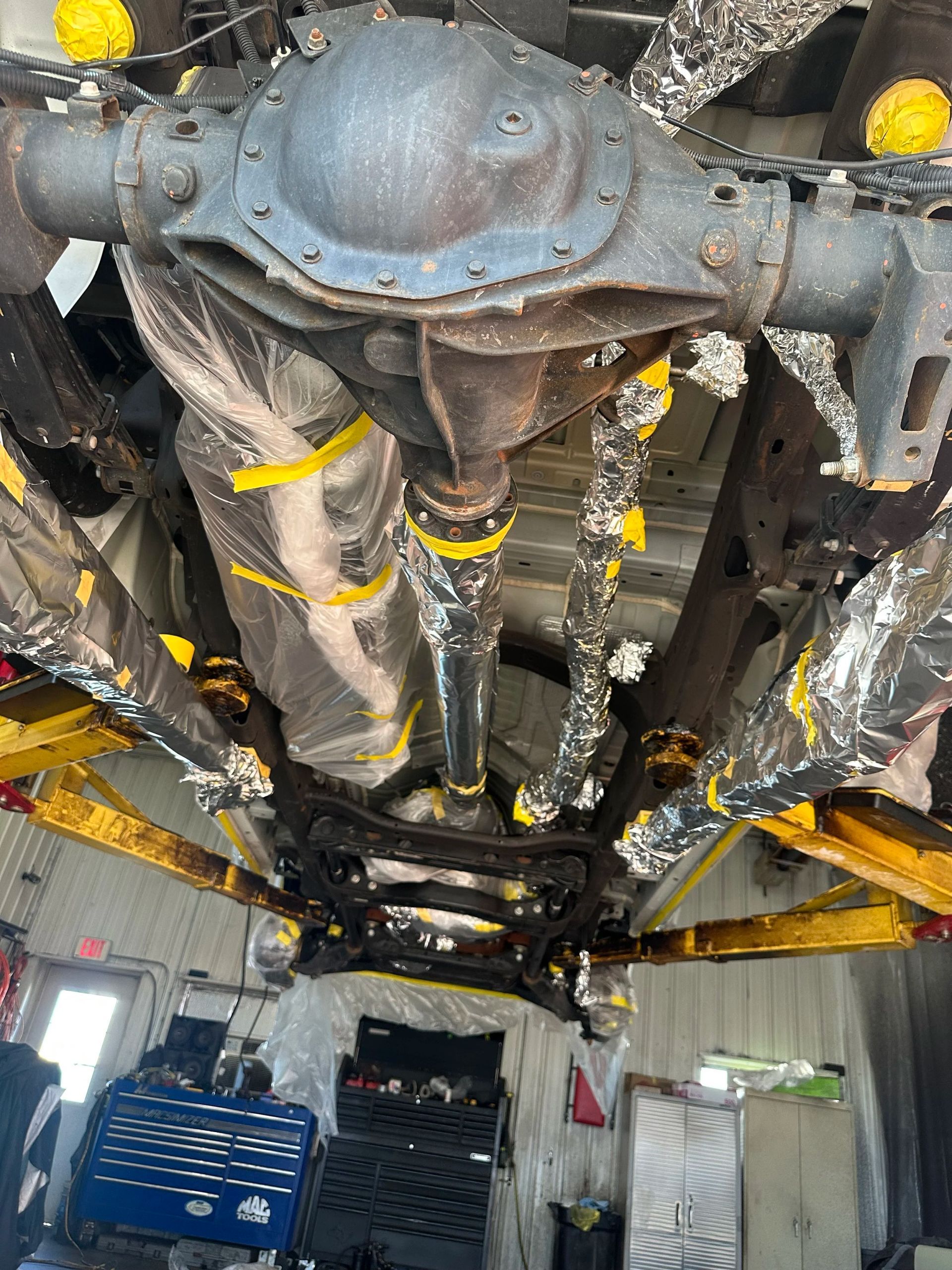 Undercarriage of a vehicle on a lift, showing the axle and drivetrain in a workshop