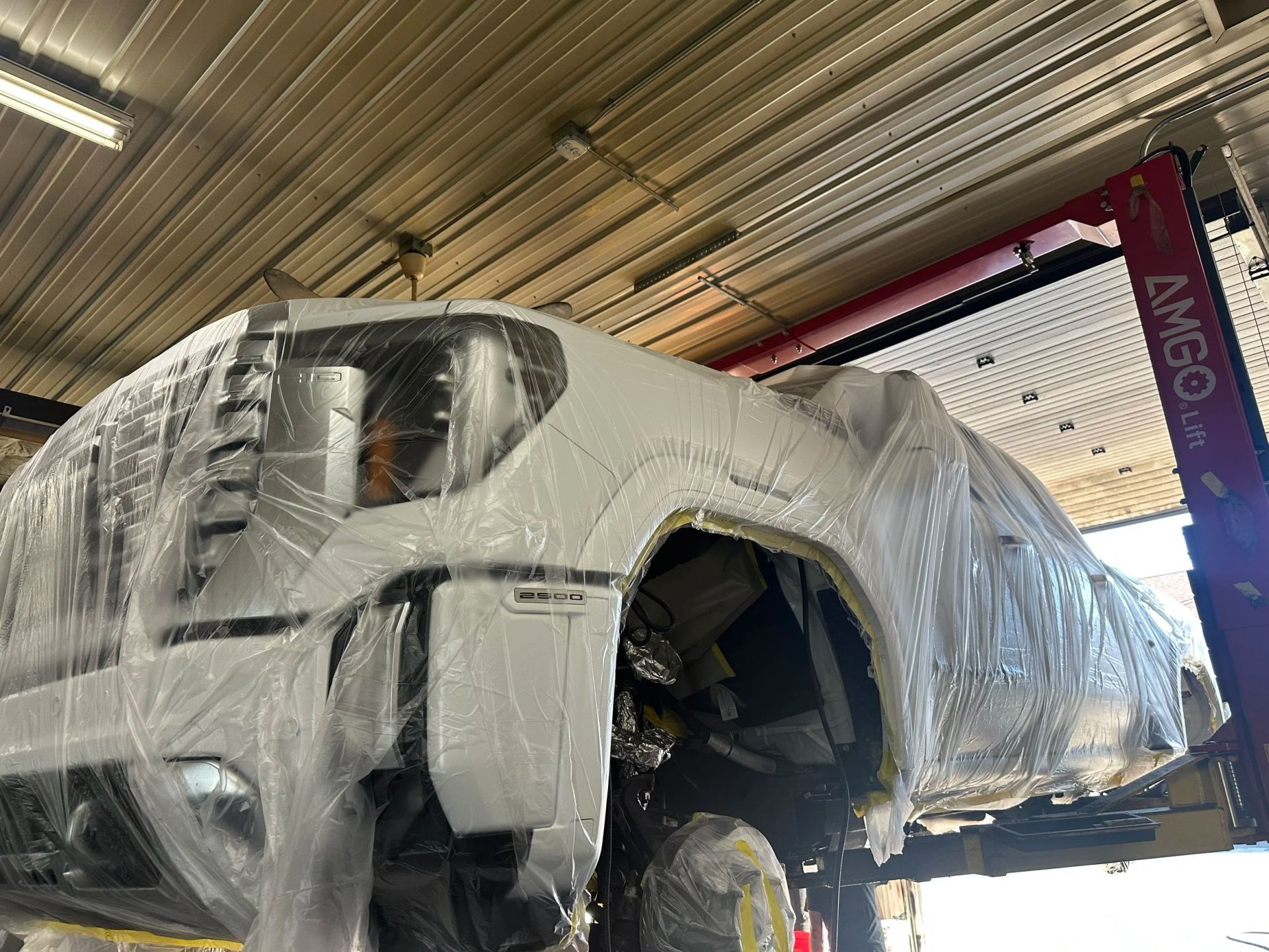 Wrapped car body in a workshop, suspended under clear plastic sheeting during repair or paint preparation