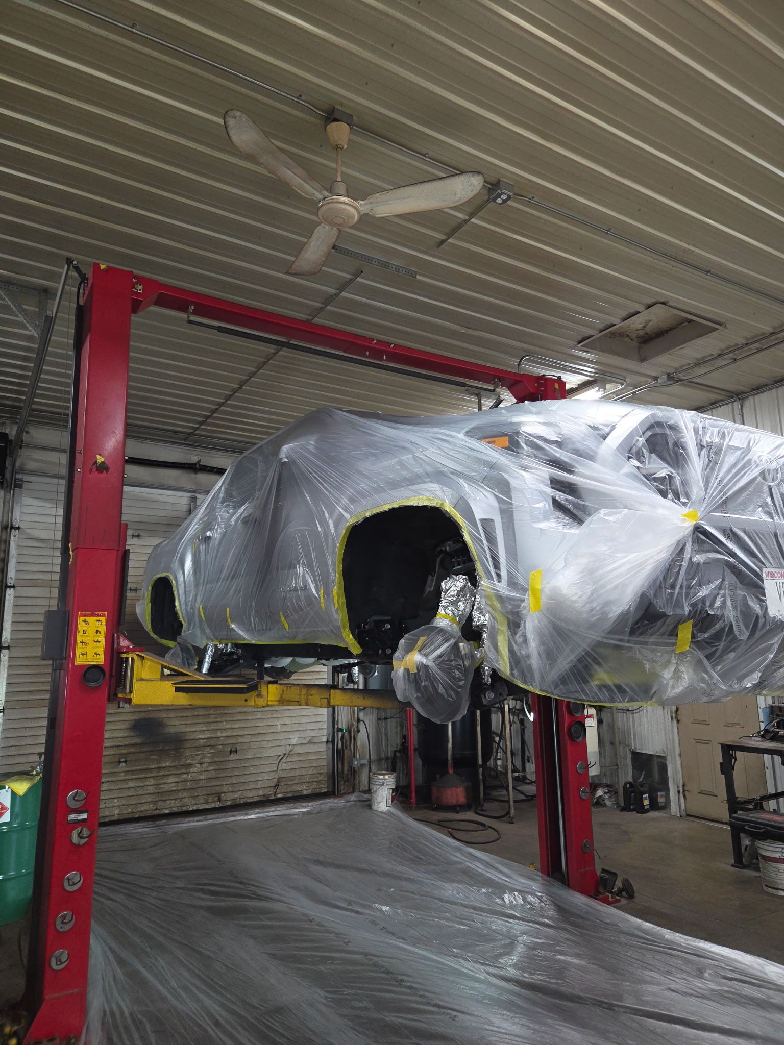 Car wrapped in plastic on a red lift inside an auto repair shop