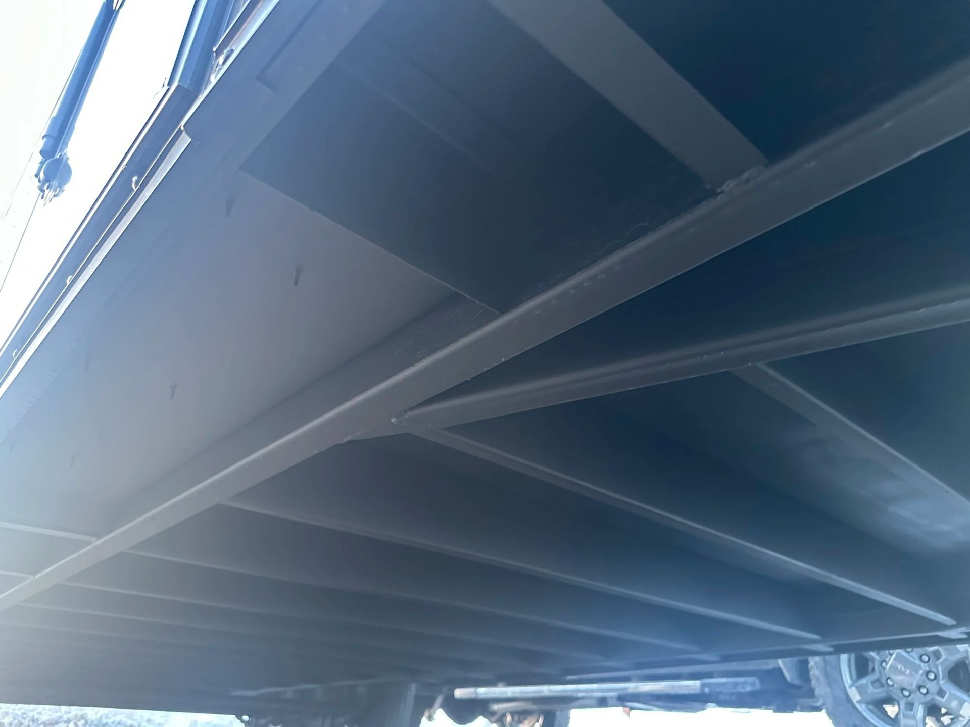 Underside of a blue steel bridge or overpass with beams and sunlight streaming in from the left