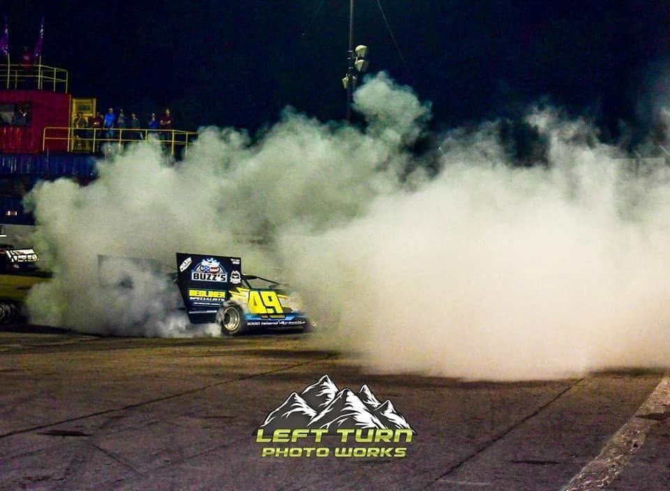 Race car drifting through thick smoke at night on a track, with a bright yellow sponsor logo.