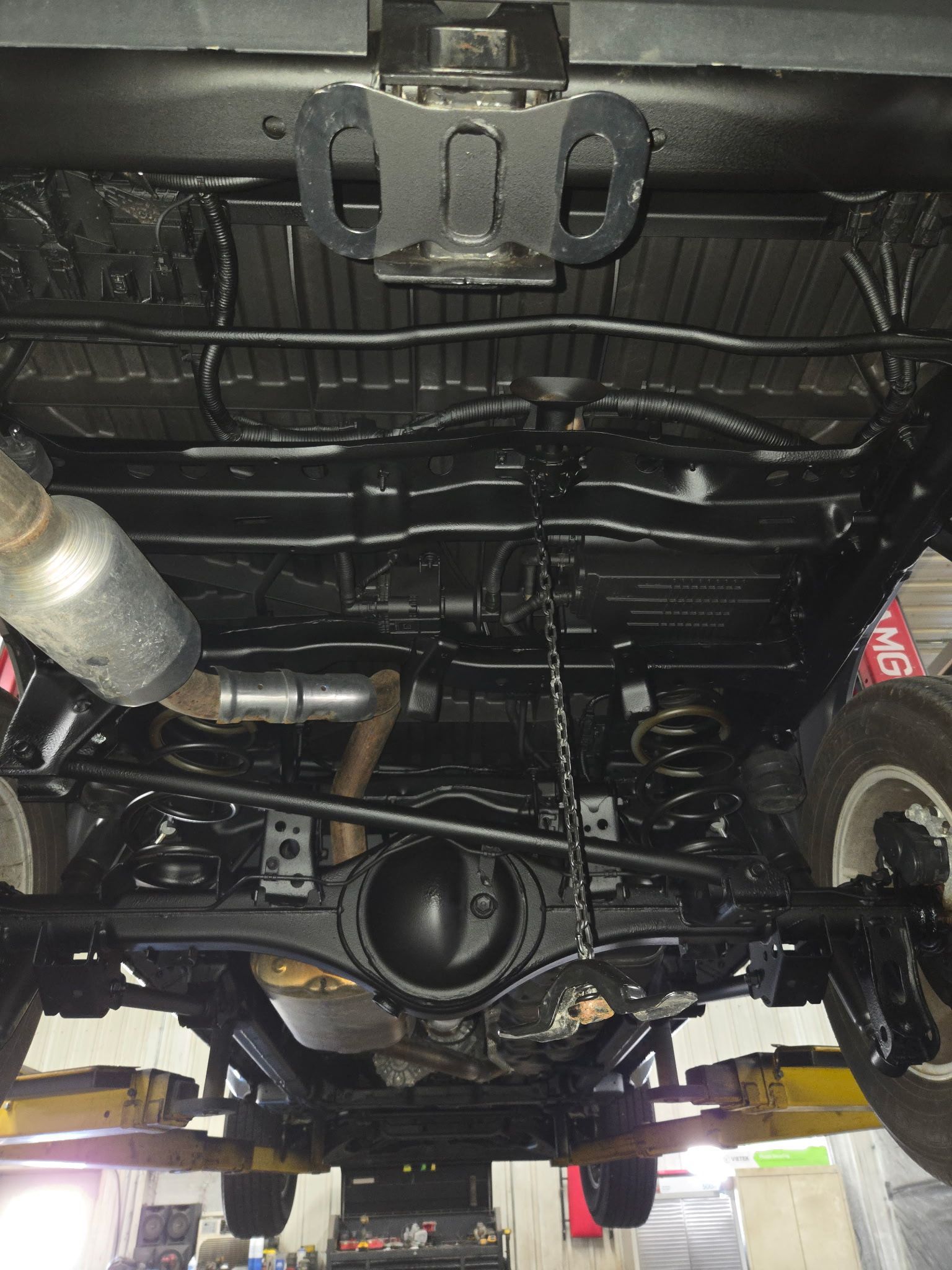 Undercarriage of a vehicle on a lift, showing exhaust, suspension, and differential components.