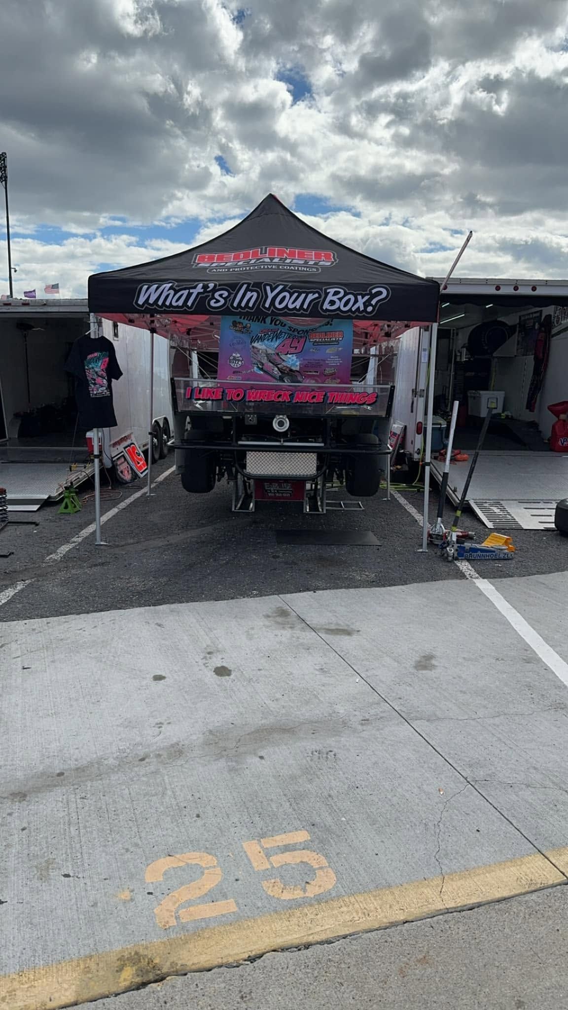 Festival booth with black canopy, pink banner, and equipment set up in a parking space under cloudy skies