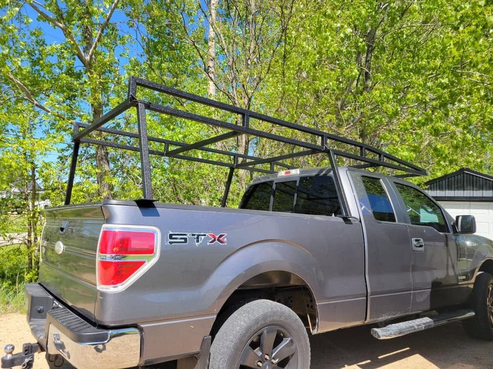 Gray pickup truck with a black metal rack parked outdoors among trees and greenery