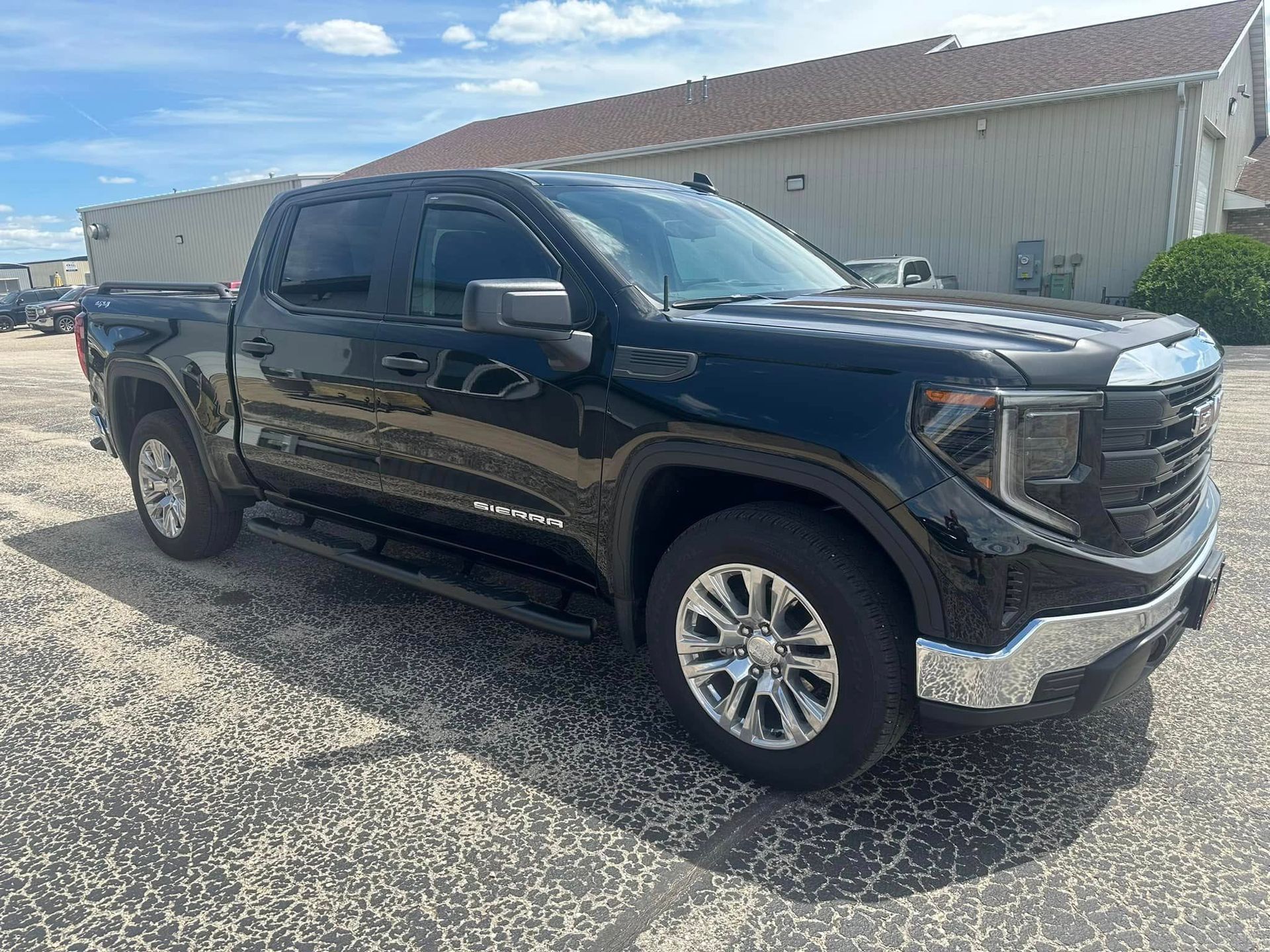 Black GMC pickup truck parked on a gravel lot beside a beige building in bright sunlight