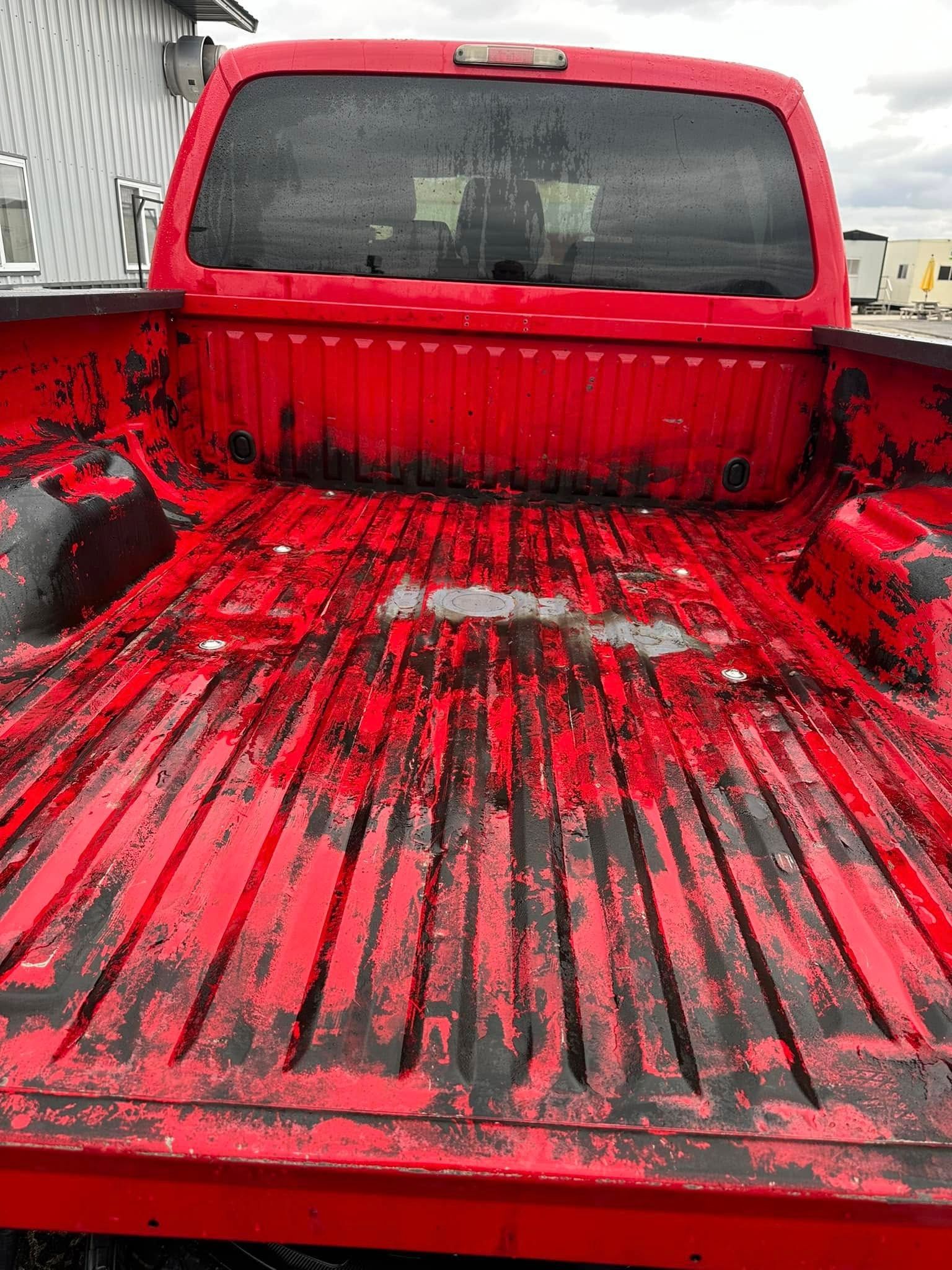 Red pickup truck bed covered in black and white splatter, viewed from the tailgate.