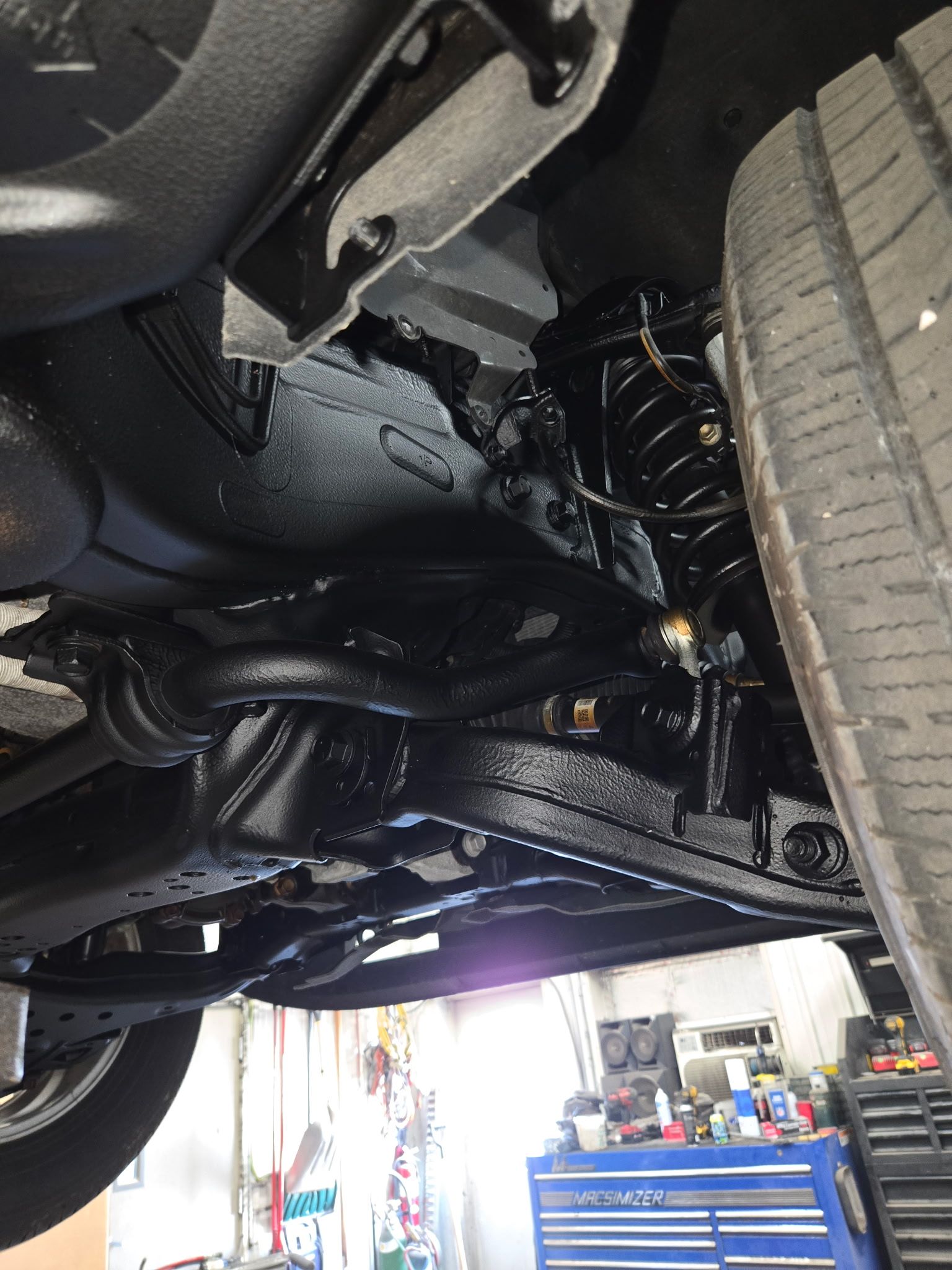 Undercarriage of a car in a garage, showing suspension and rear tire close-up.