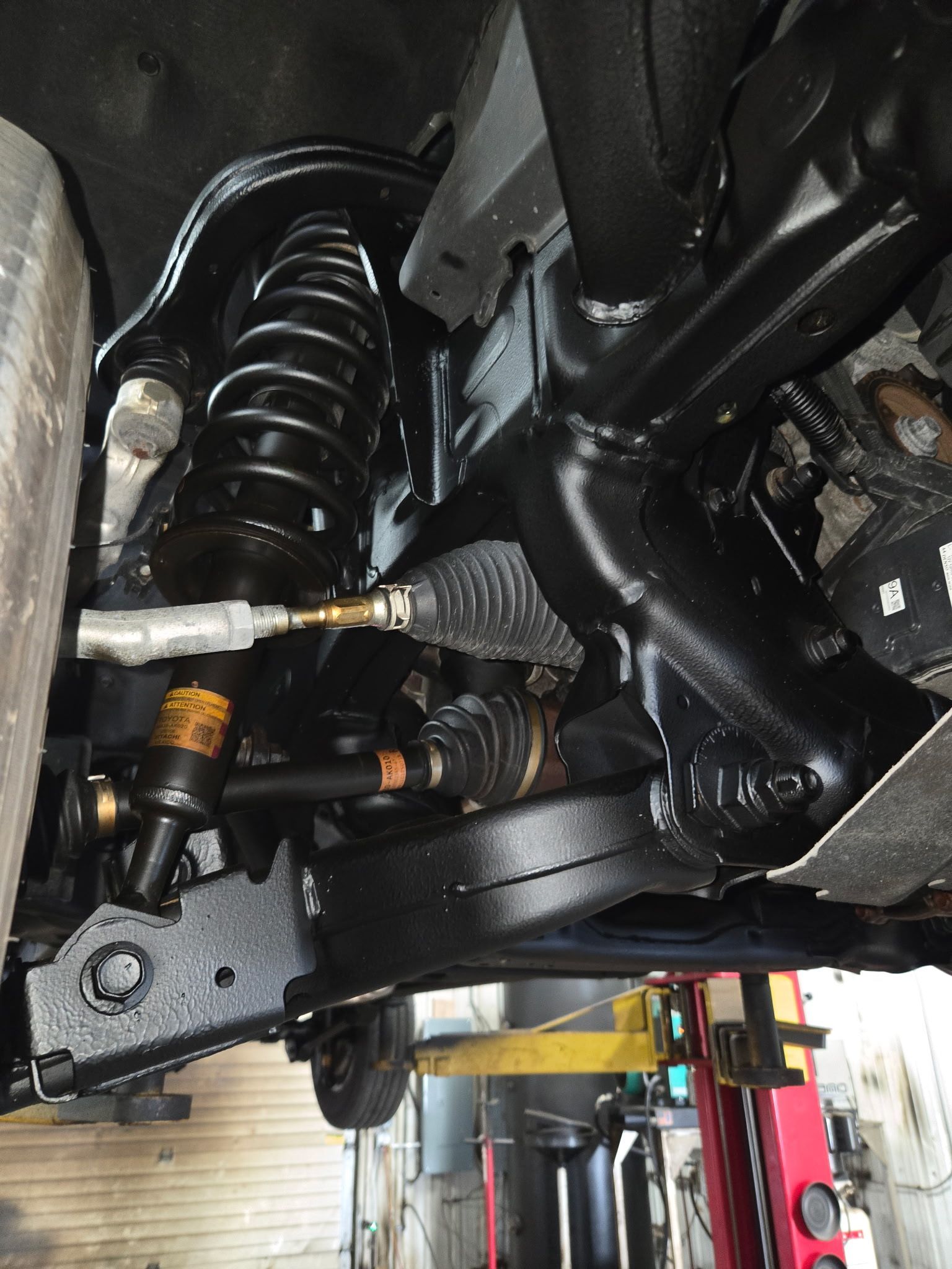 Undercarriage of a vehicle showing suspension, coil spring, axle, and steering components in a garage lift.