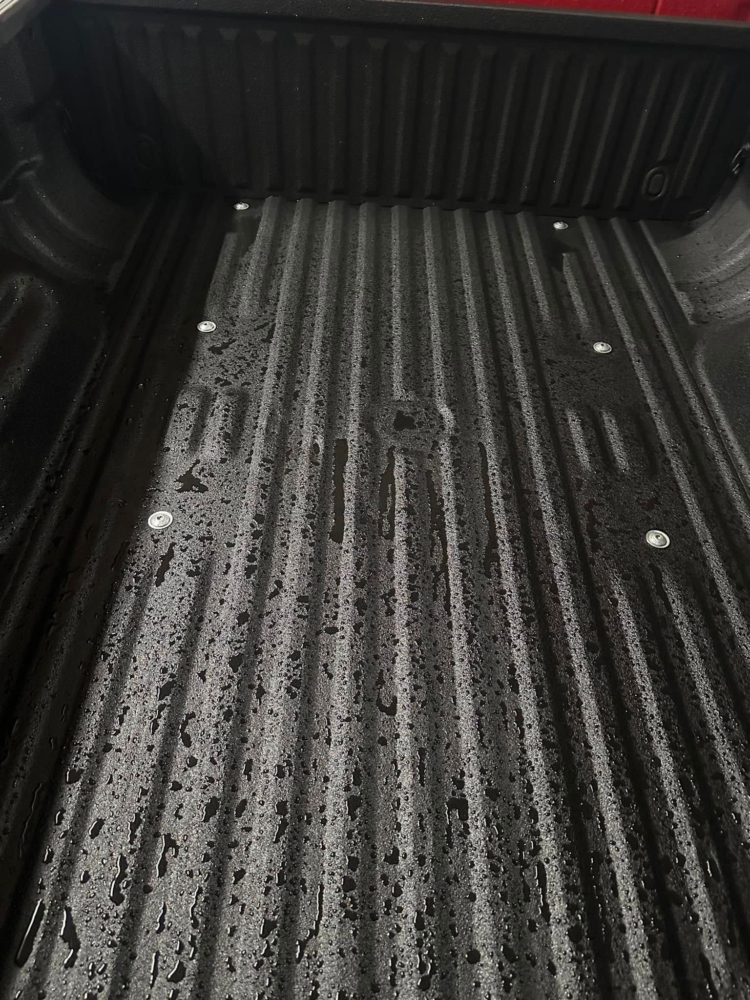 Black ridged truck bed liner with a thin layer of snow or frost across the floor.