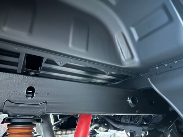 Undercarriage of a vehicle, showing suspension components and a red jack stand in a garage.