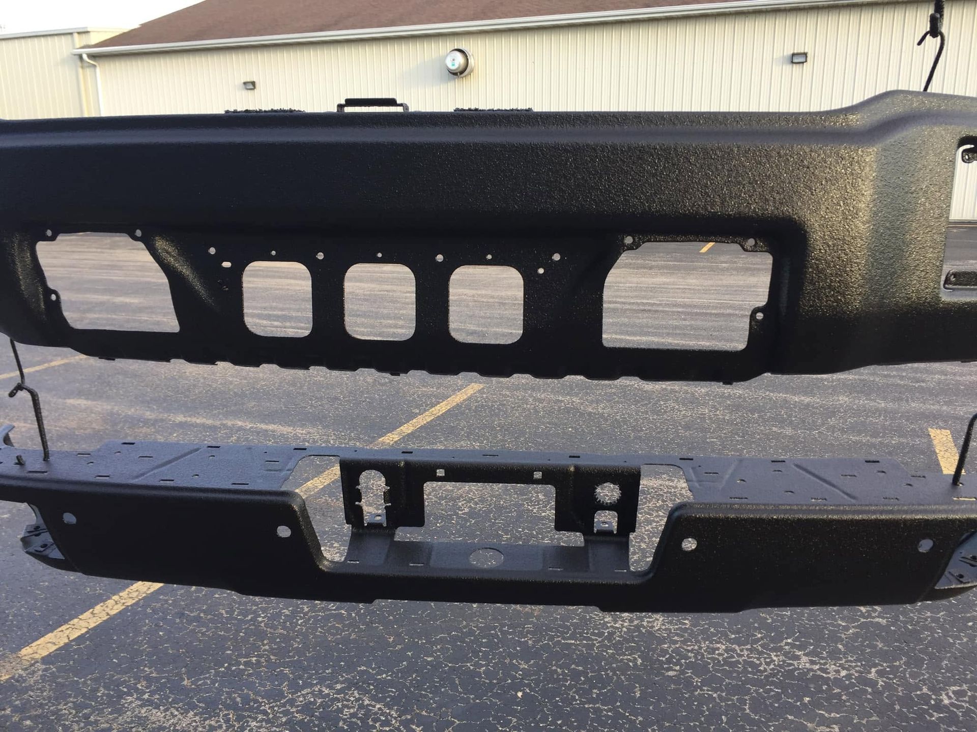 Black truck front bumper and grille assembly lying on asphalt in a parking lot
