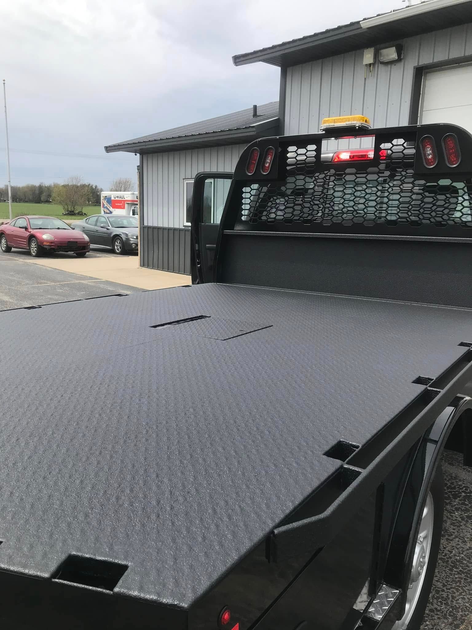 Flatbed tow truck parked beside a metal building, with a red car in the background.