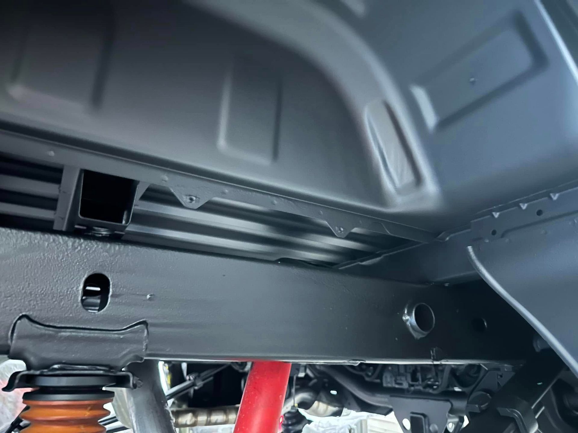 Close-up of a vehicle’s undercarriage with a red shock absorber and gray body panels