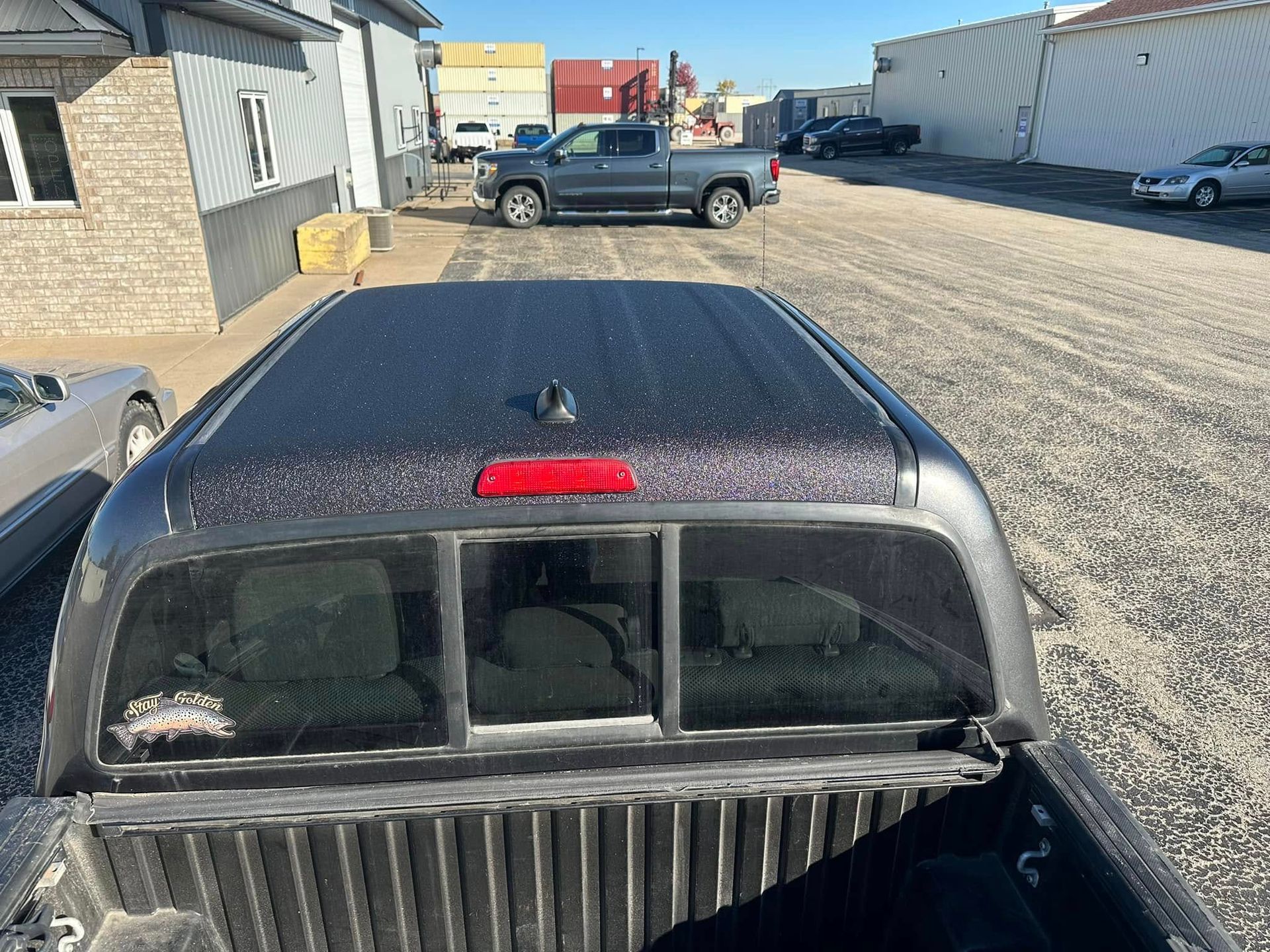 Black pickup truck with a snow-dusted roof in a gravel lot beside industrial buildings