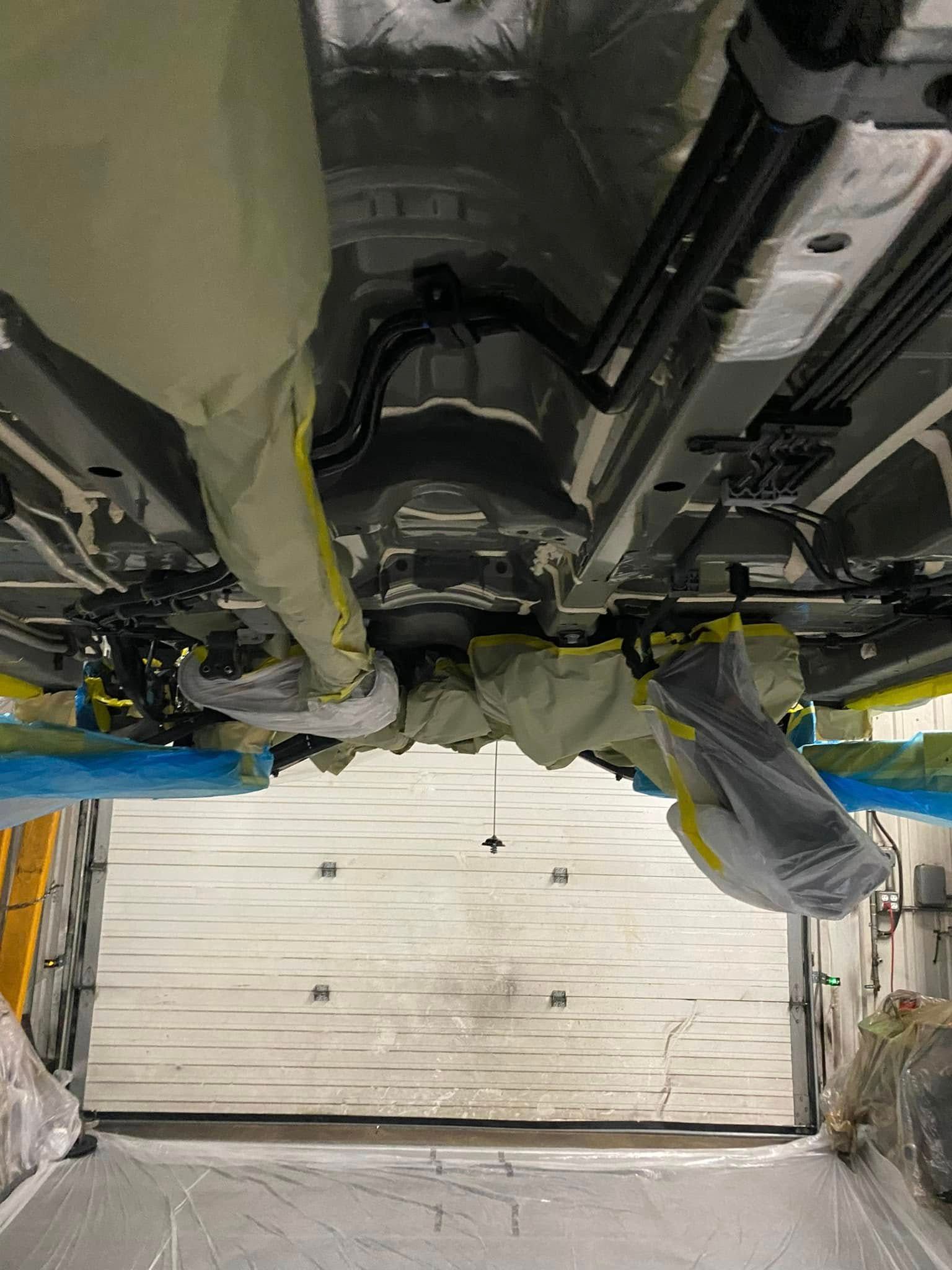 Undercarriage of a vehicle on a lift, showing mechanical components and a garage bay below.