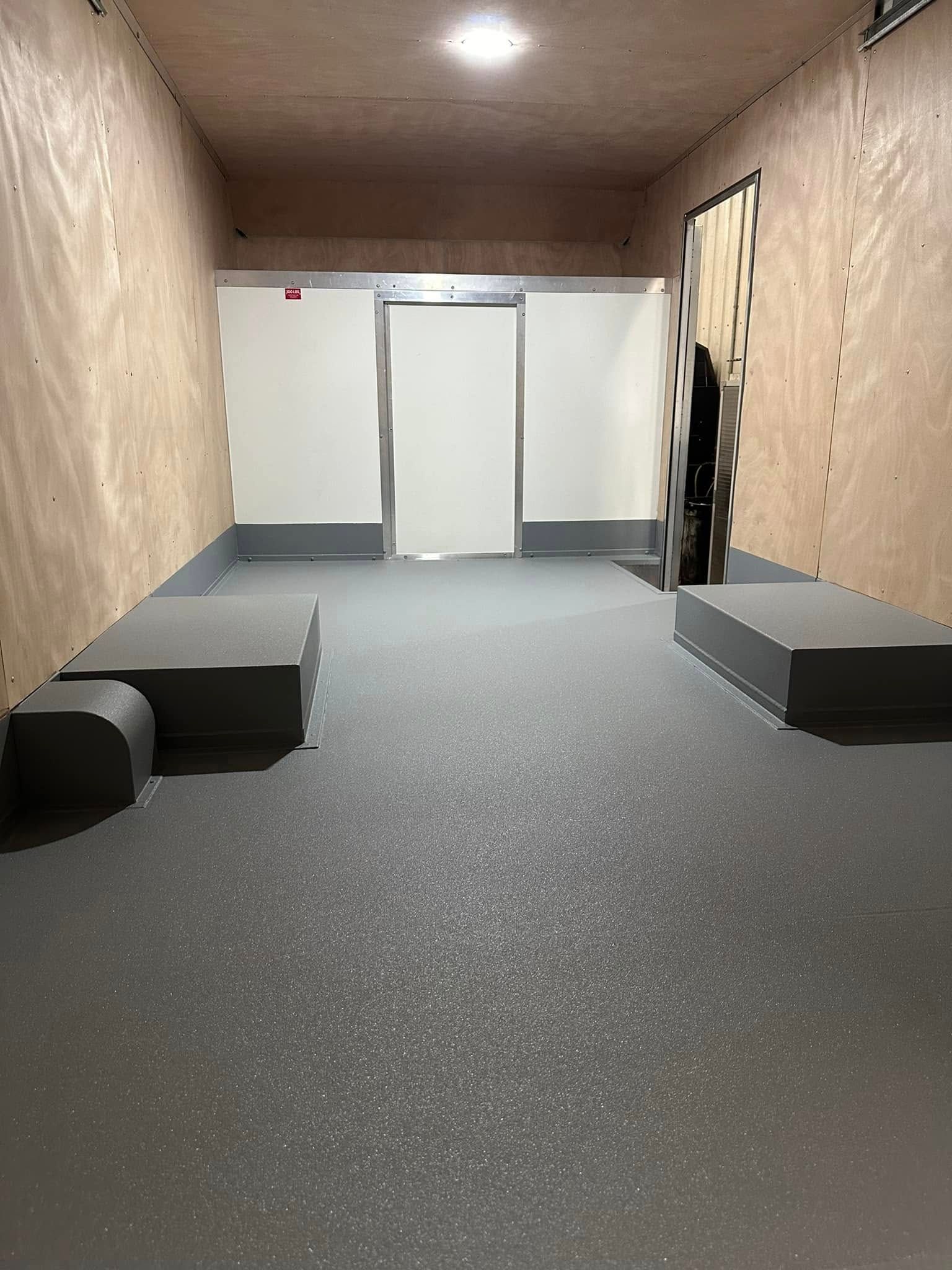 Empty indoor room with gray carpet, wood-paneled walls, white door, and low black and gray benches