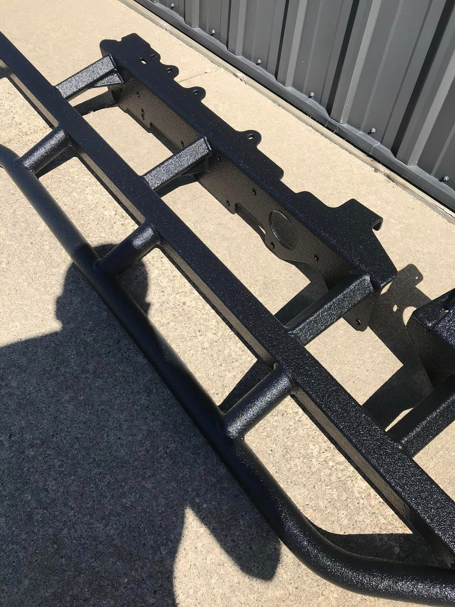 Black metal rack lying on sunlit pavement beside a corrugated metal wall.