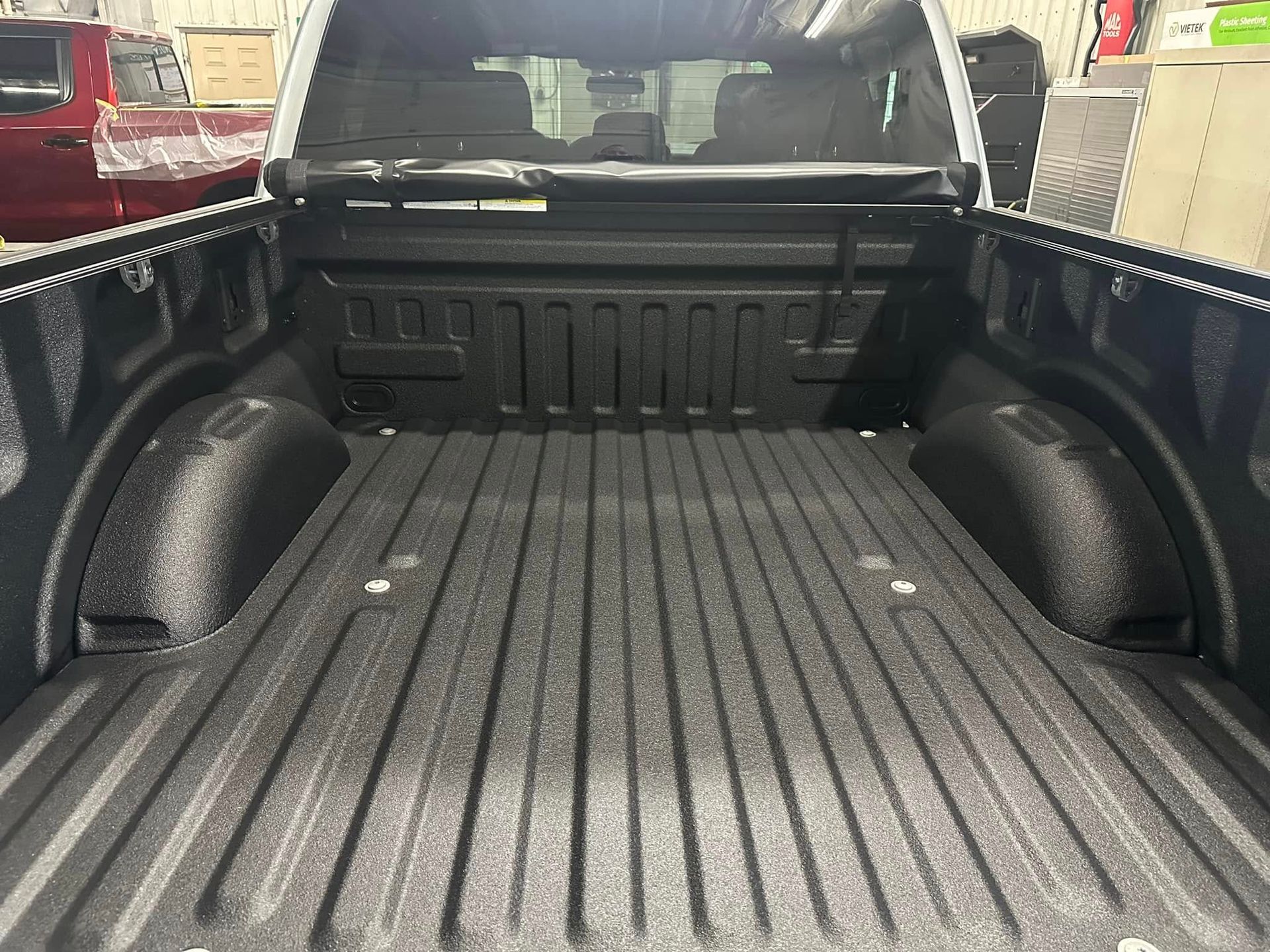 Empty black pickup truck bed with ridged liner, viewed from the tailgate inside a garage