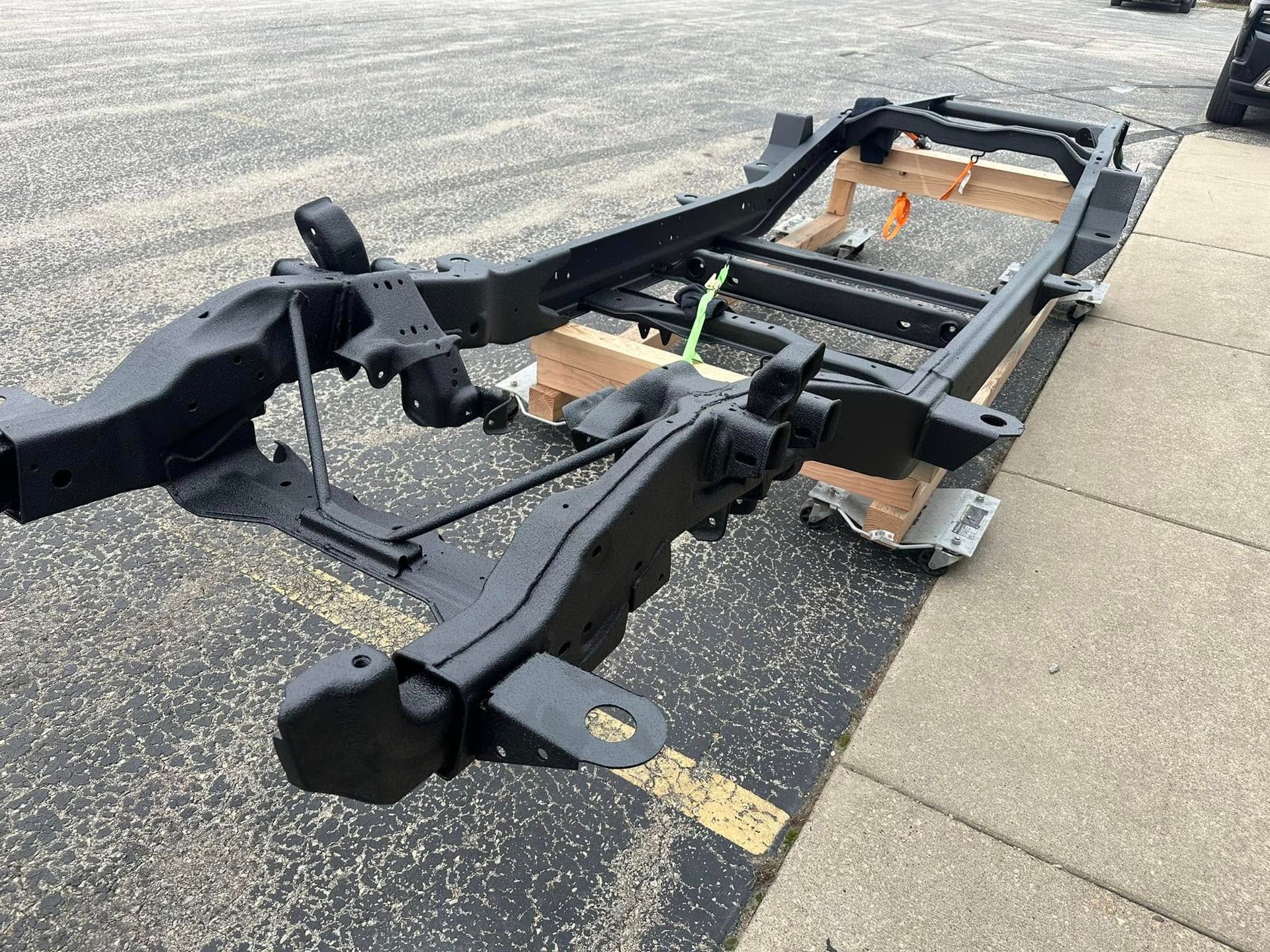 Damaged black car chassis frame lying on pavement beside a sidewalk.